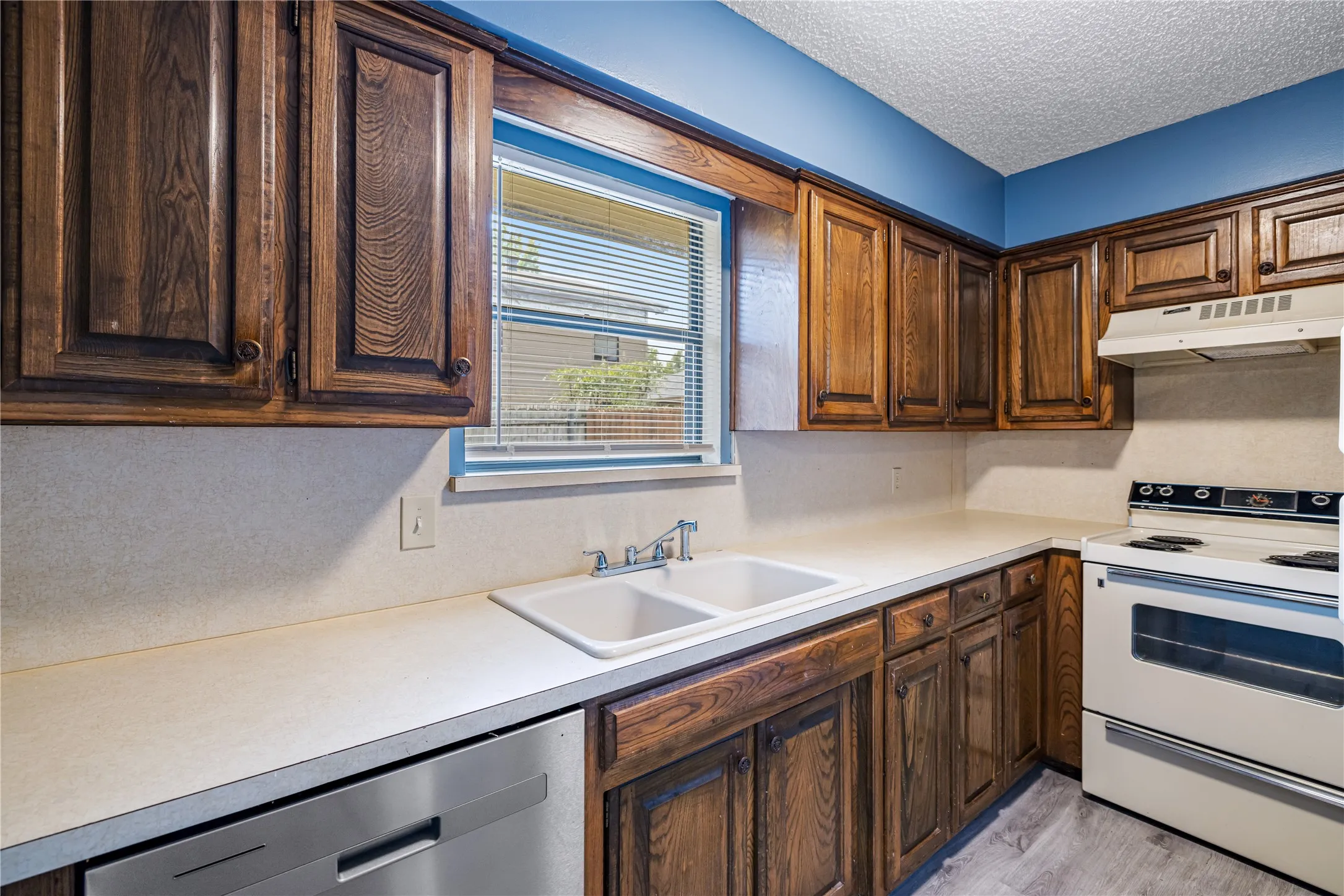 Kitchen with white range with electric cooktop, under cabinet range hood, a sink, a textured ceiling, and dishwasher
