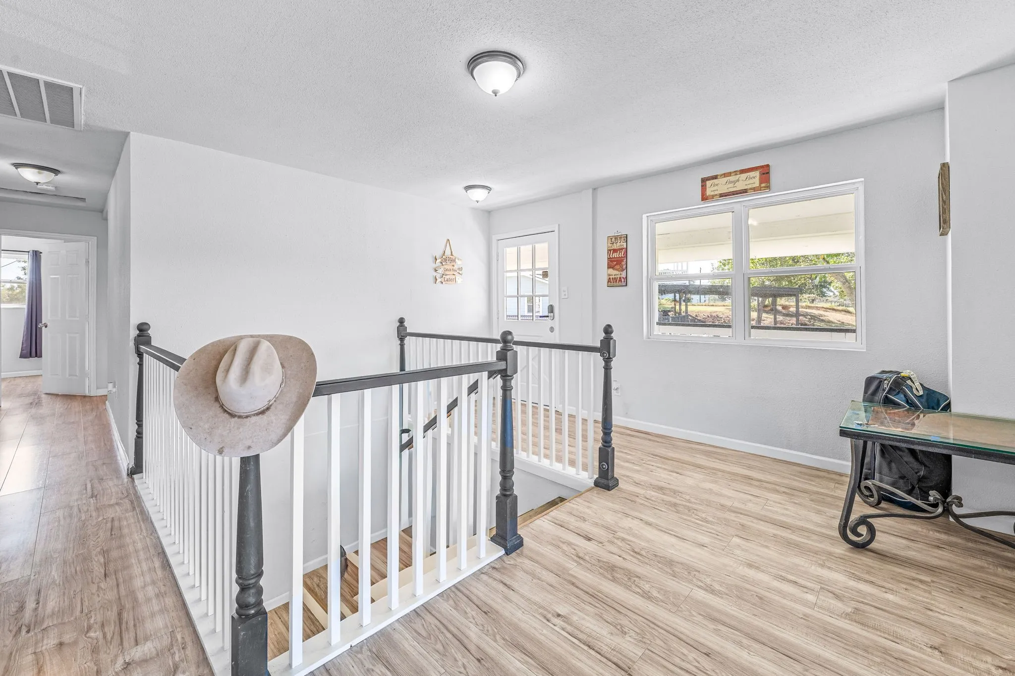 Corridor with an upstairs landing, light wood-type flooring, healthy amount of natural light, and a textured ceiling