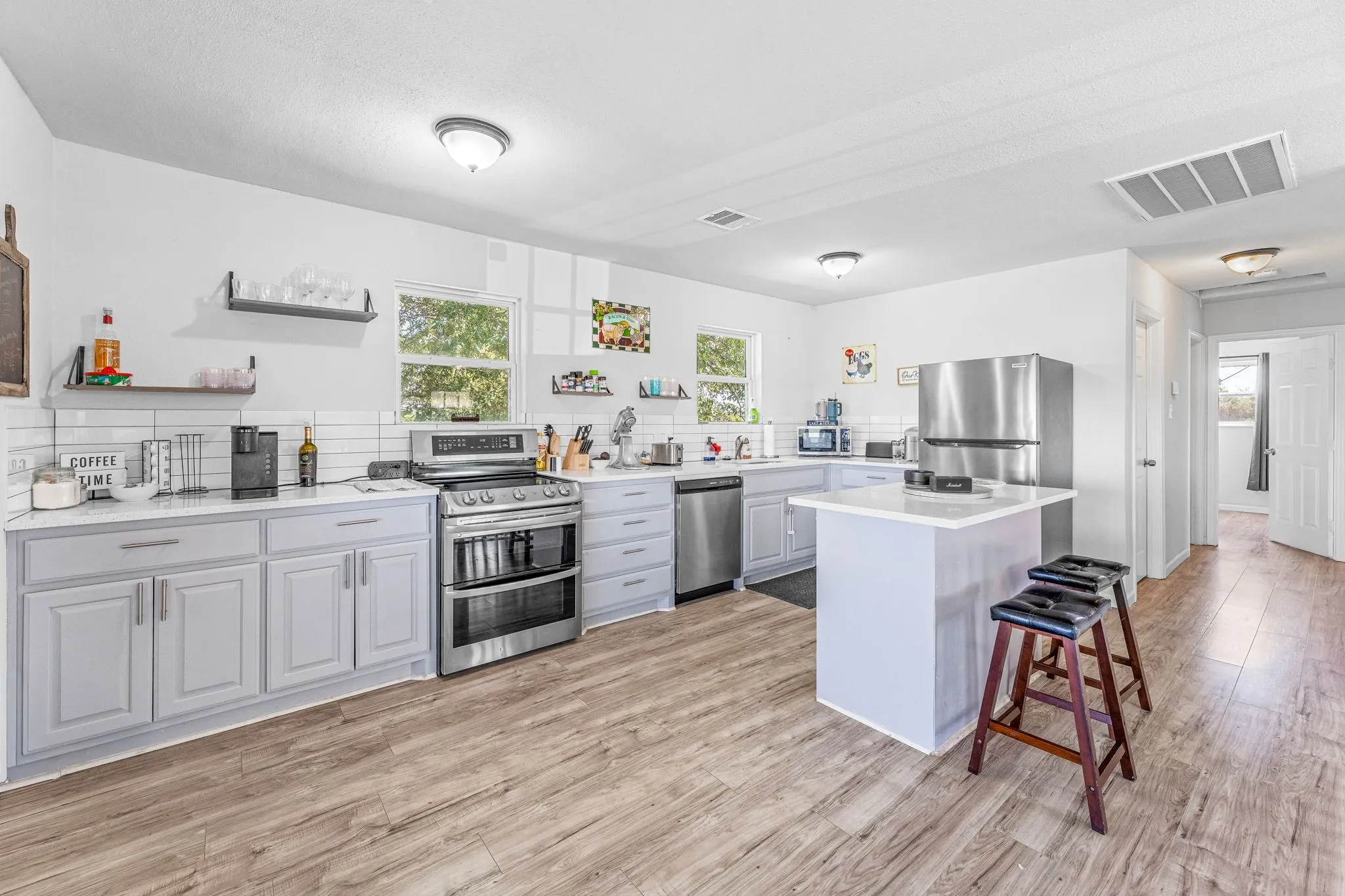 Kitchen featuring appliances with stainless steel finishes, open shelves, light wood-type flooring, a breakfast bar, and a center island
