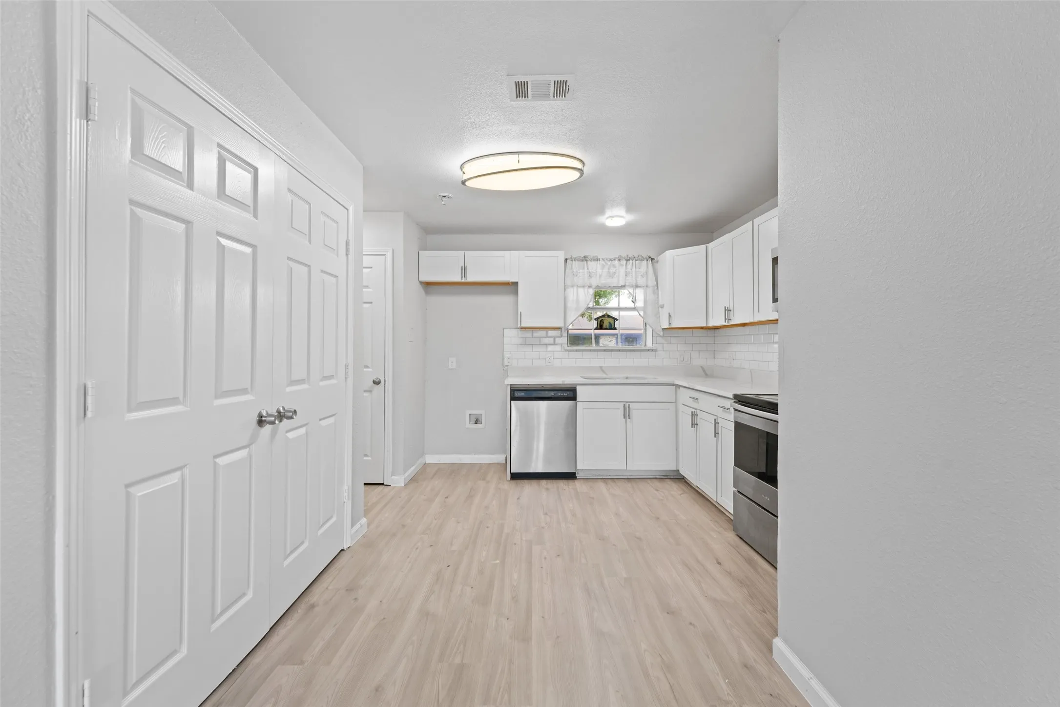 Bright kitchen featuring wood-finish flooring and white cabinetry