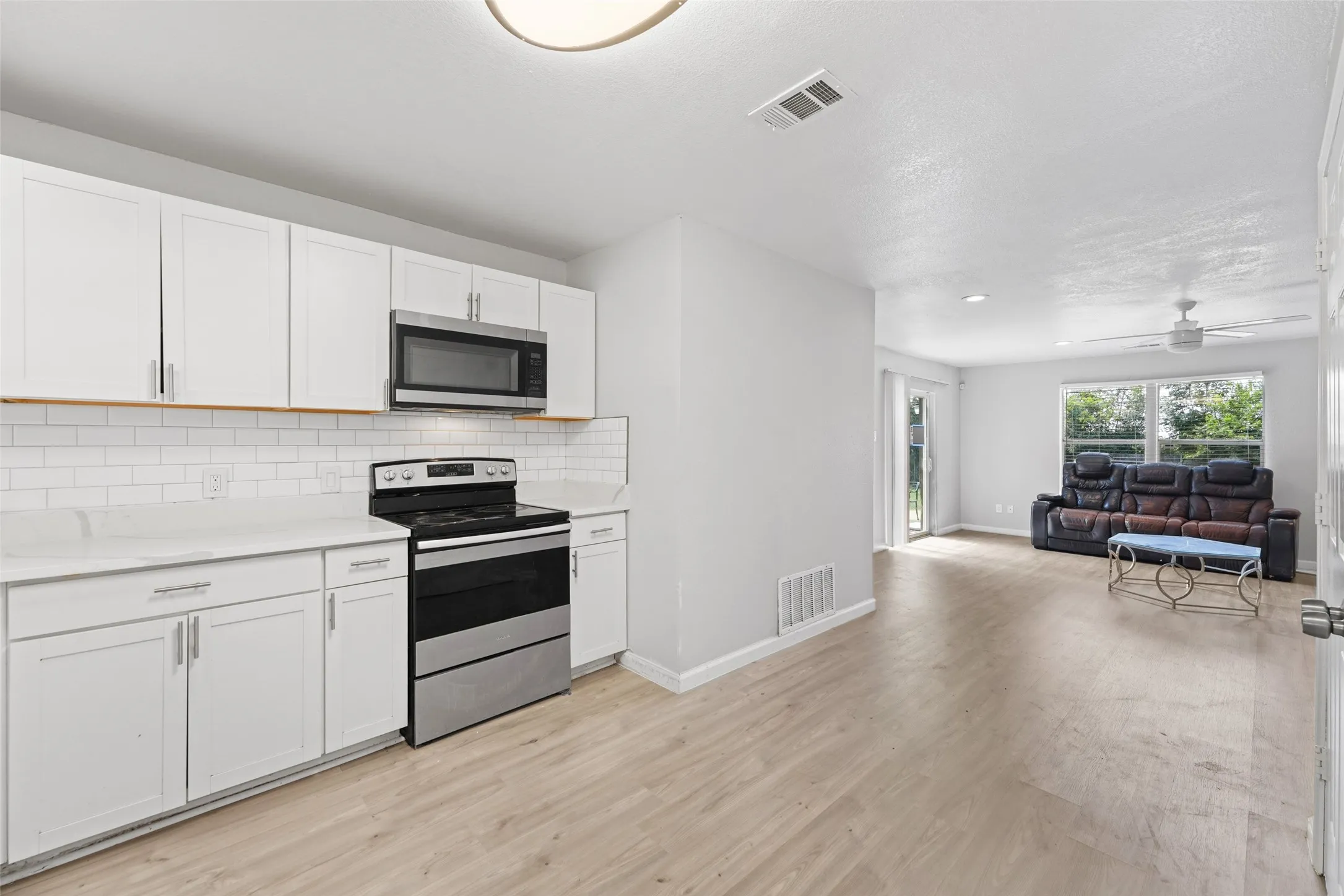 Contemporary kitchen featuring white cabinetry, subway tile backsplash, stainless steel appliances, and light wood-finish flooring