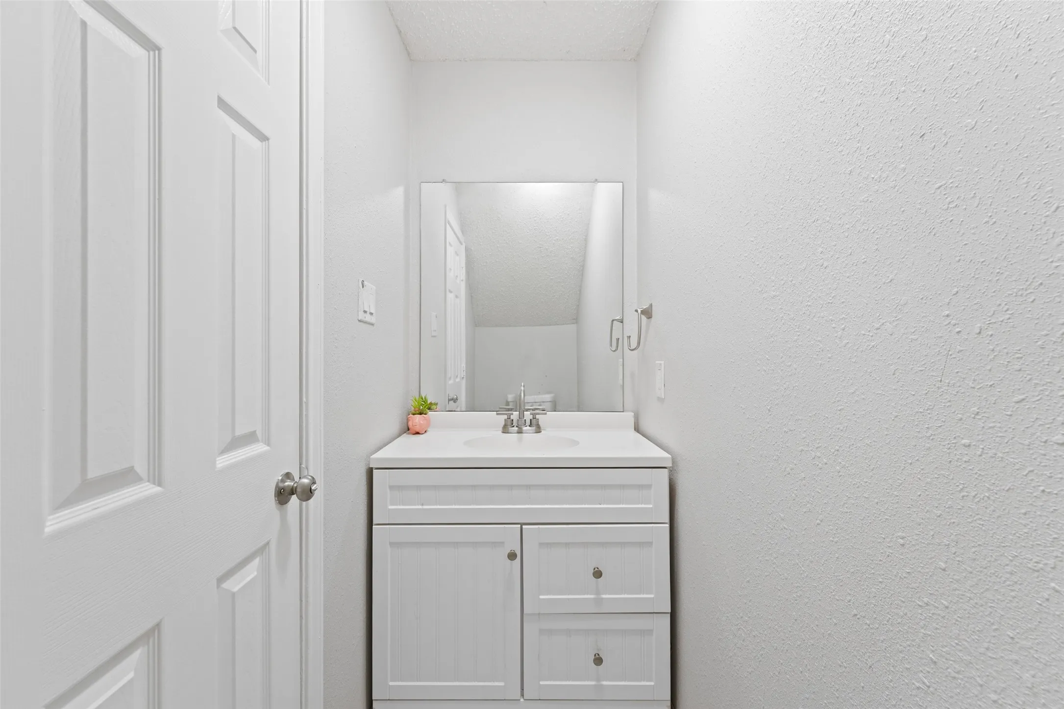 White panel door entry to a bathroom featuring a vanity with a white countertop, an integrated sink, and brushed chrome hardware