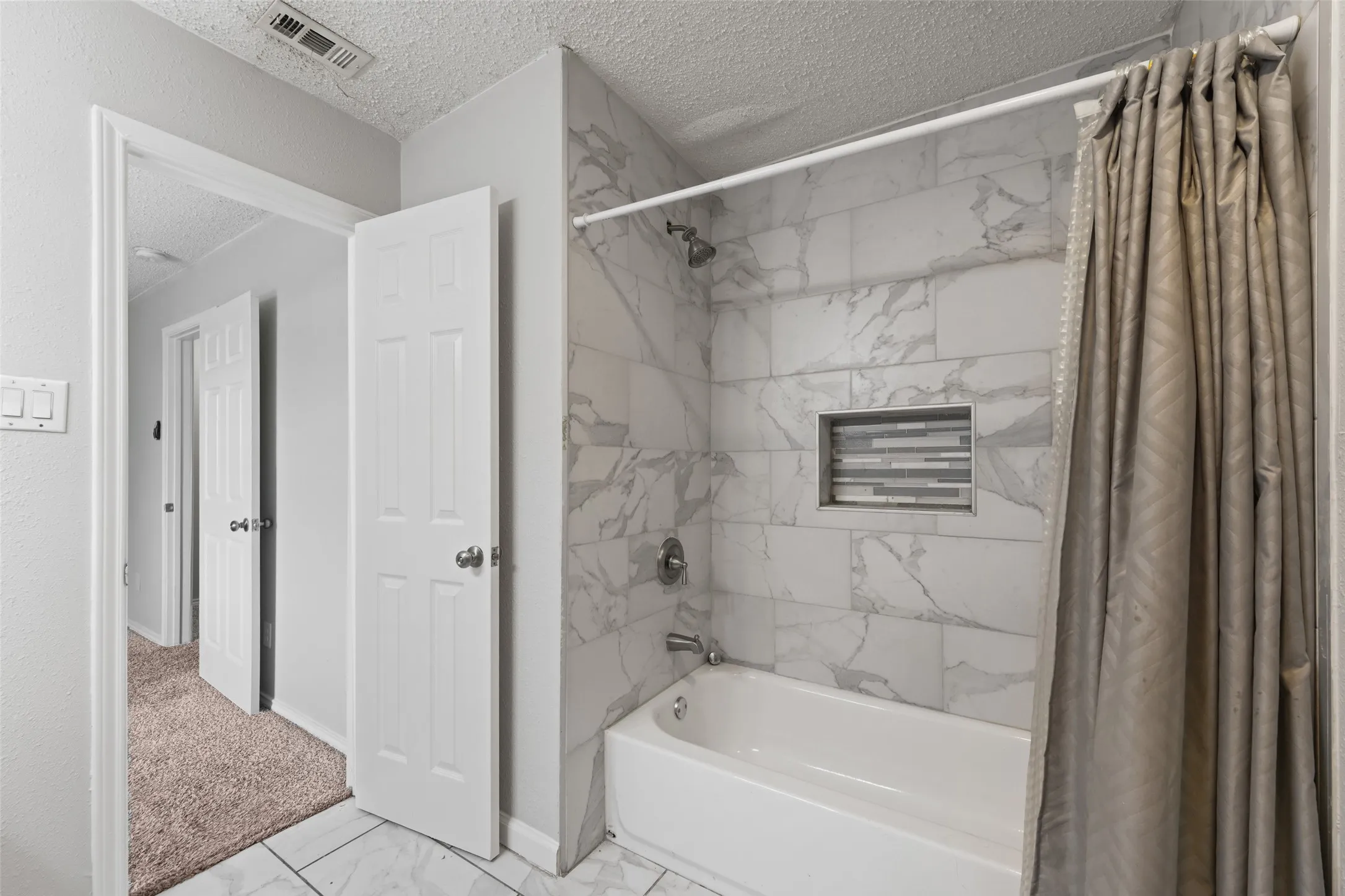 Bathroom featuring a white subway tile shower surround with grey veining, a built-in mosaic tile niche, and a white bathtub