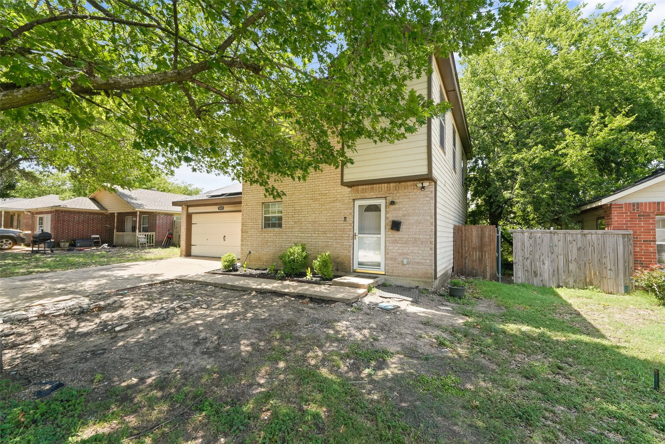 Two-story property featuring a brick and siding exterior, an attached garage, a front entry door with a storm door, and mature trees providing shade