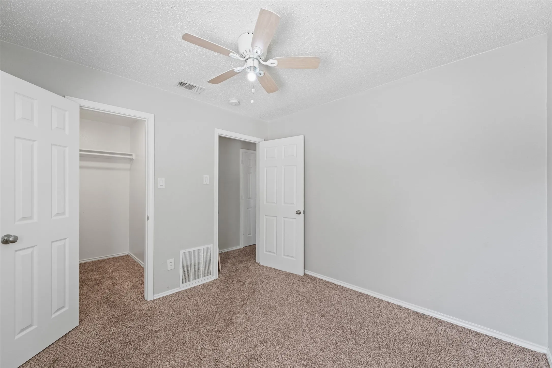 Carpeted room featuring light gray walls and a white ceiling fan with light-colored blades