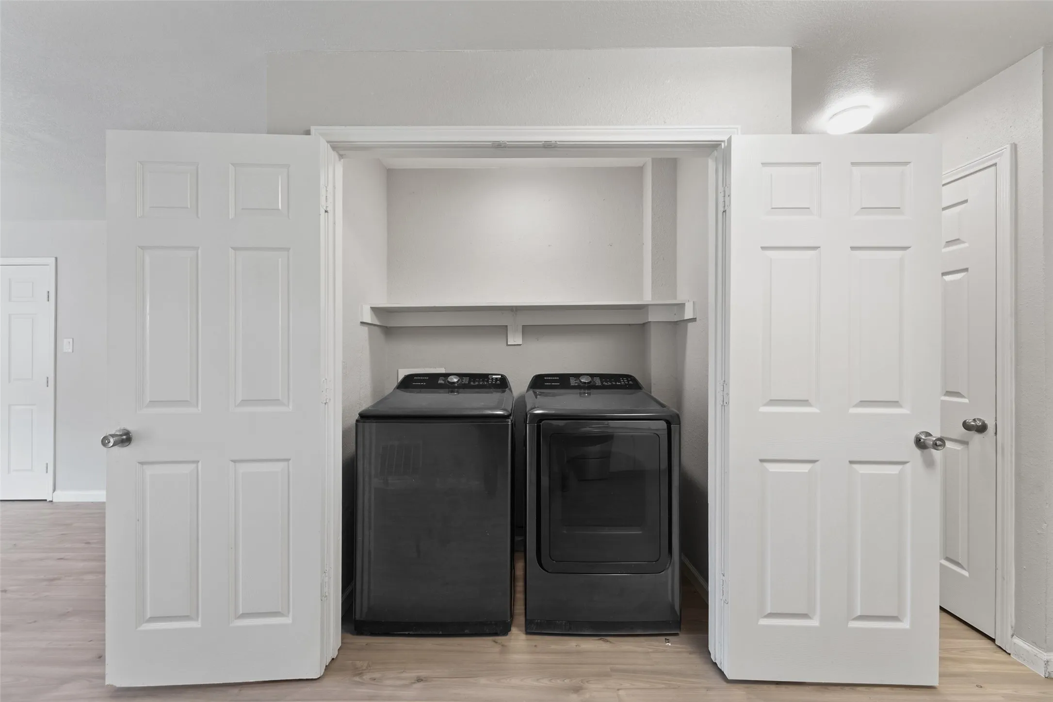 Laundry closet featuring bi-fold doors, wood-finish flooring, and a built-in shelf