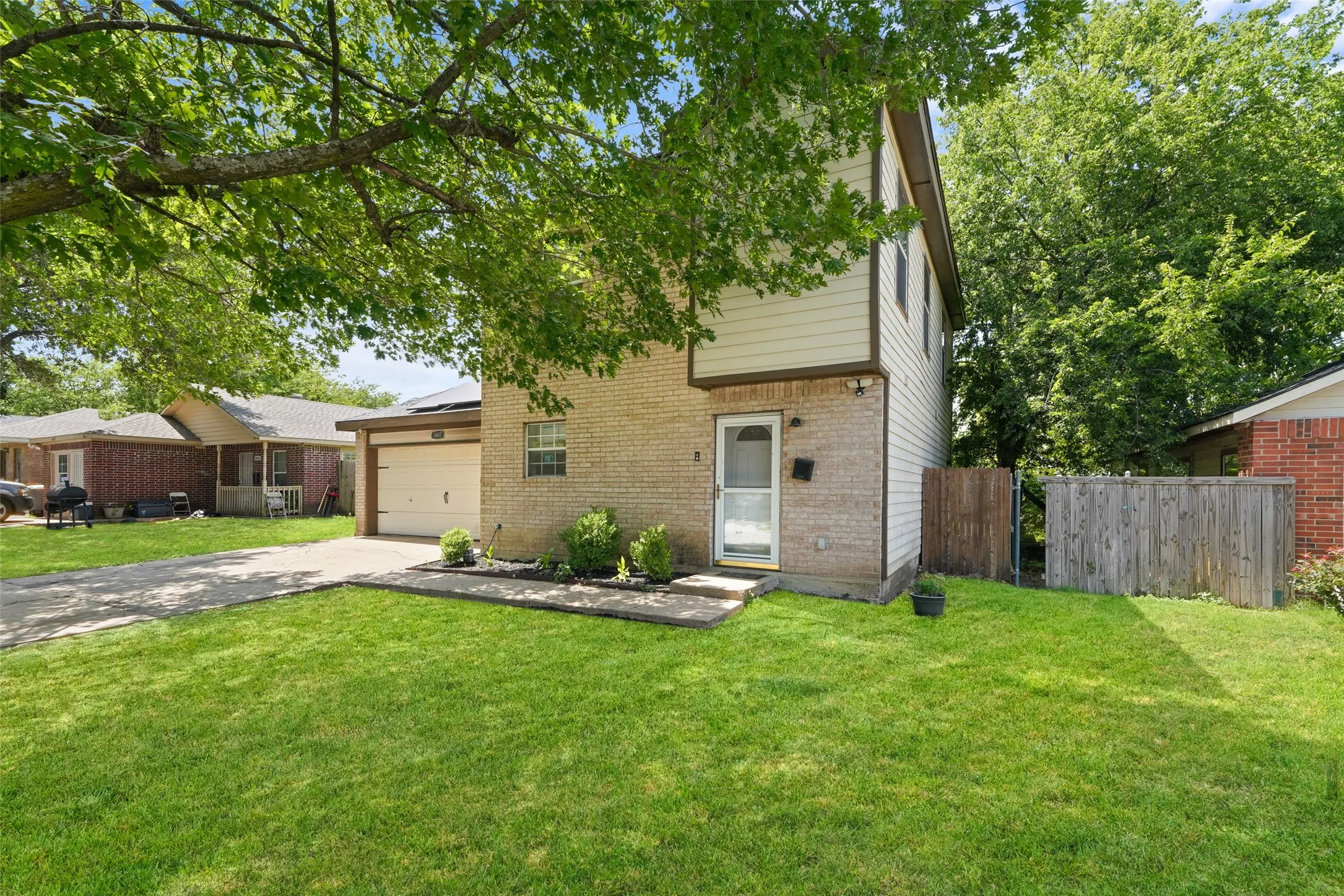 Two-story residence featuring a brick and siding exterior, an attached garage, a front entry door with a storm door, and mature trees providing shade