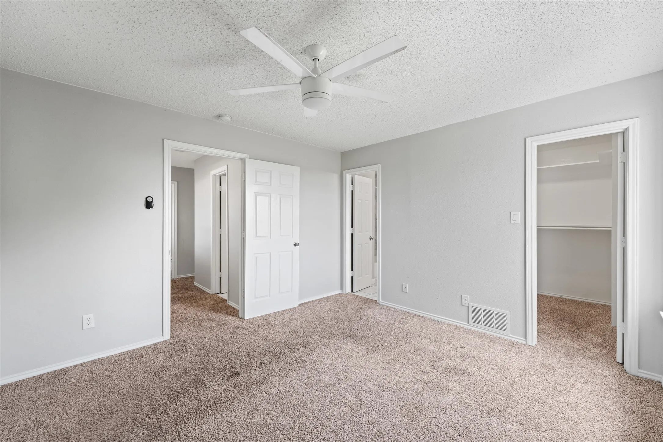 Room featuring neutral tone carpeting, light gray walls, a white ceiling fan, and multiple white paneled doors