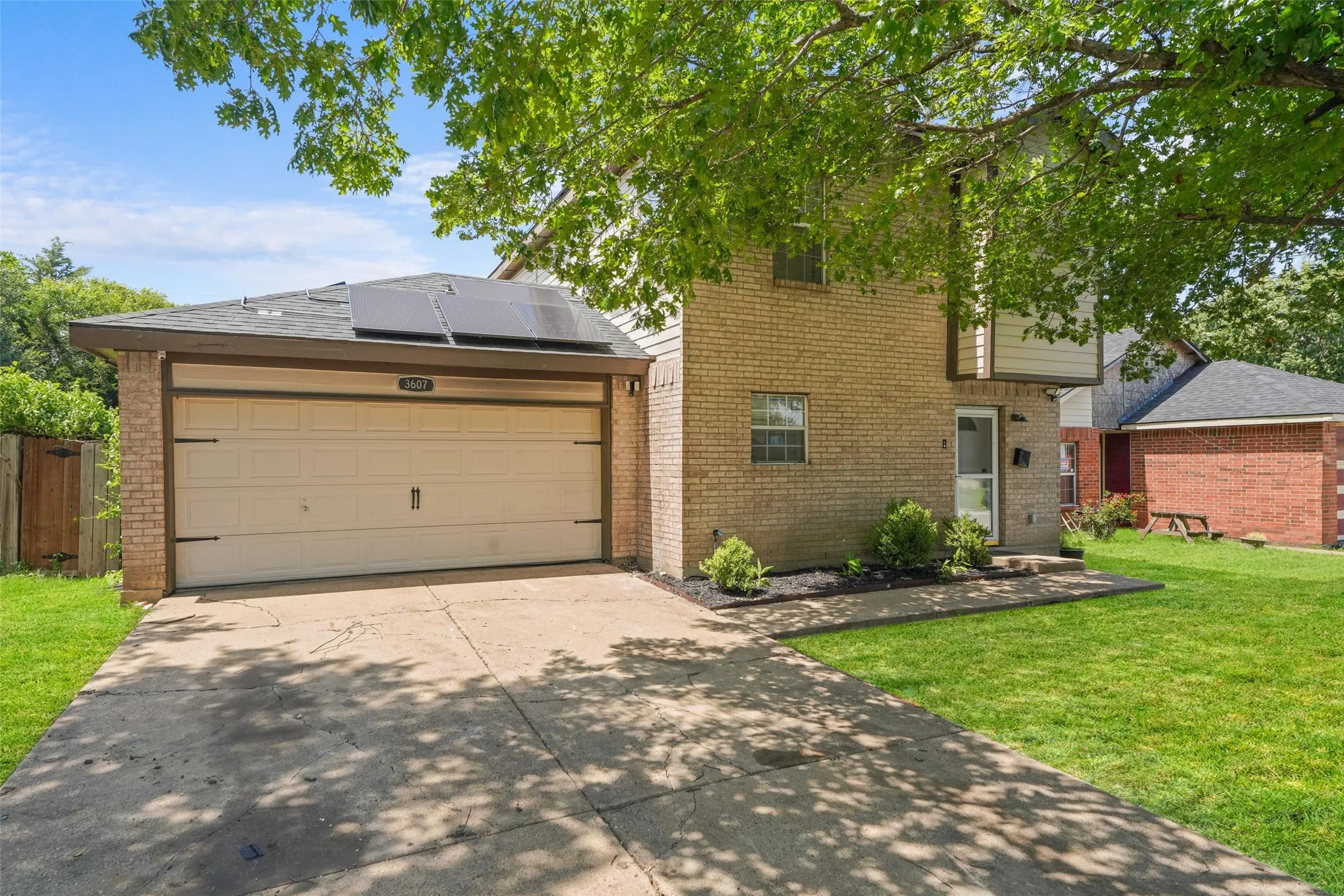 Brick exterior featuring a two-car garage with a panel door, solar panels on the garage roof, a concrete driveway, and a manicured lawn