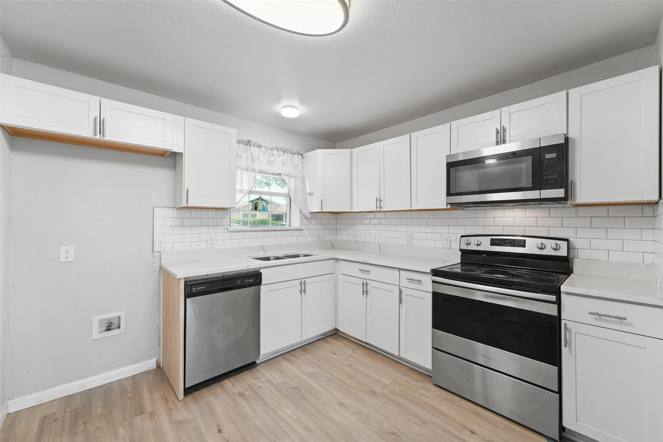Kitchen featuring white cabinetry, light countertops, subway tile backsplash, stainless steel appliances, and wood-finish flooring