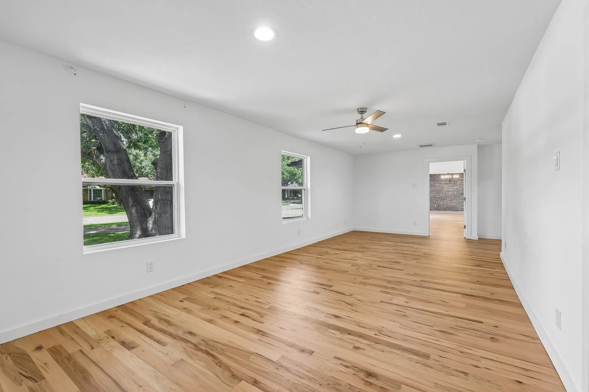 Spacious room featuring wood-finish flooring, white walls, and multiple windows