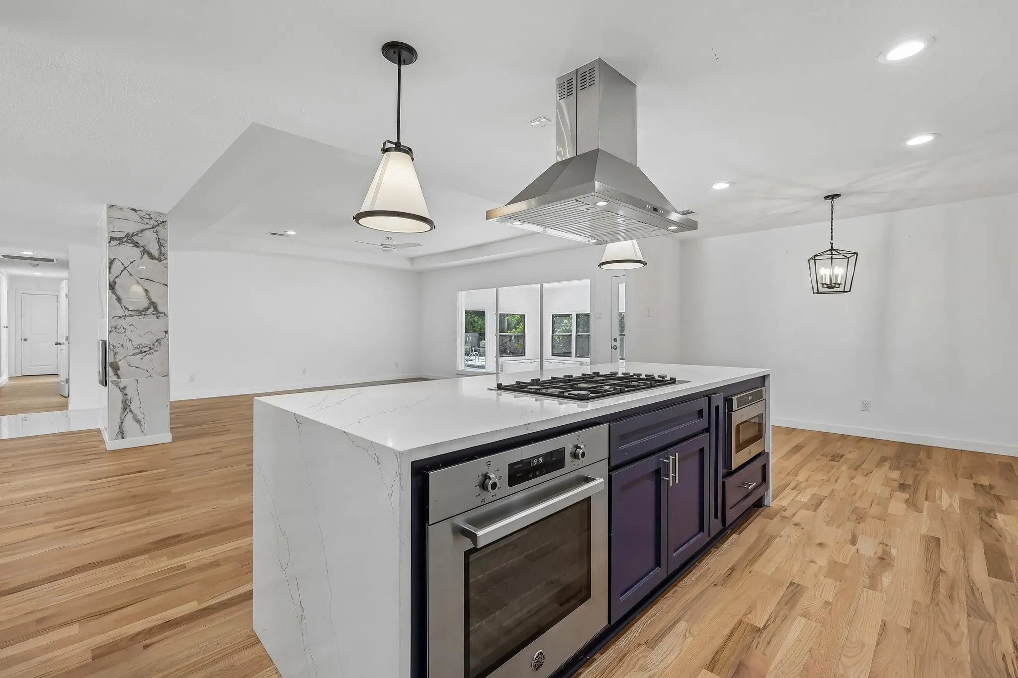 Kitchen island featuring a quartz waterfall countertop, integrated gas cooktop, stainless steel oven, and microwave