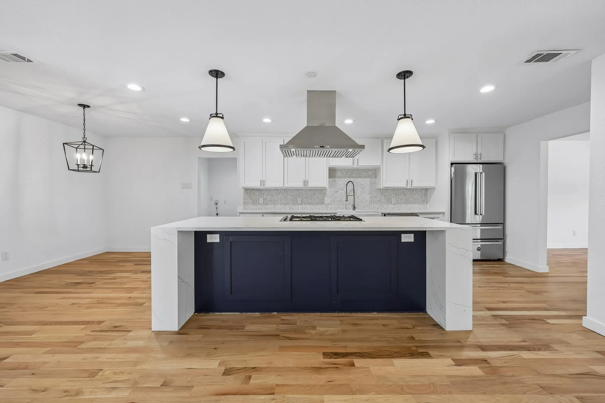 Kitchen featuring a waterfall-edge island with deep blue cabinetry, stainless steel appliances, a gas range, and pendant lighting