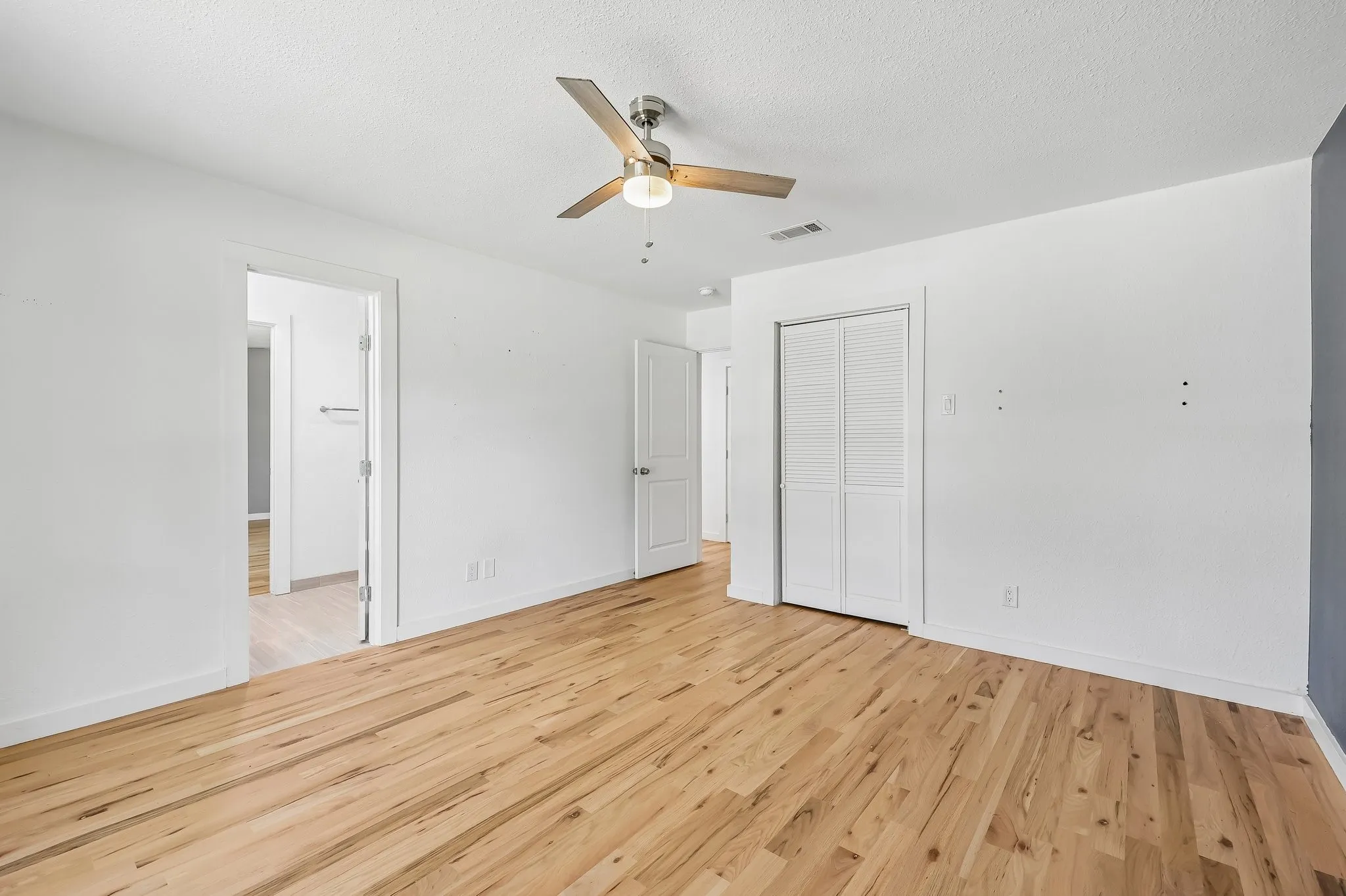 Spacious room featuring wood-finish flooring, white walls, and a ceiling fan with integrated lighting