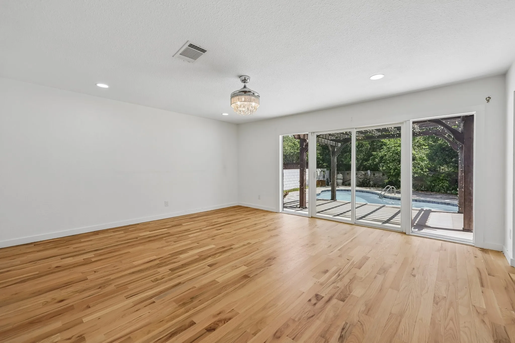 Spacious room featuring wood-finish flooring, recessed lighting, and a crystal chandelier