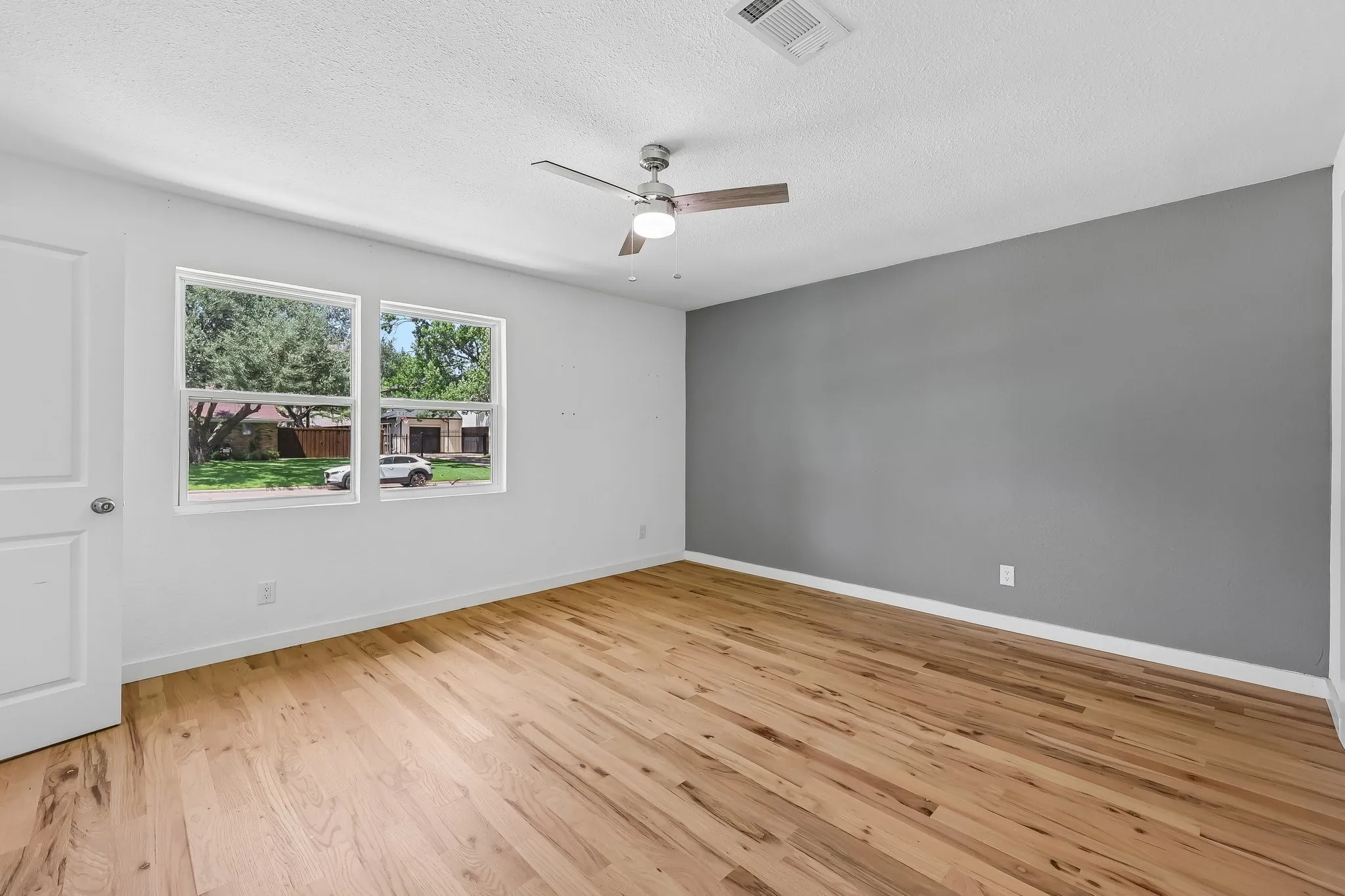 Room featuring wood-finish flooring, white walls, and a single accent wall in gray