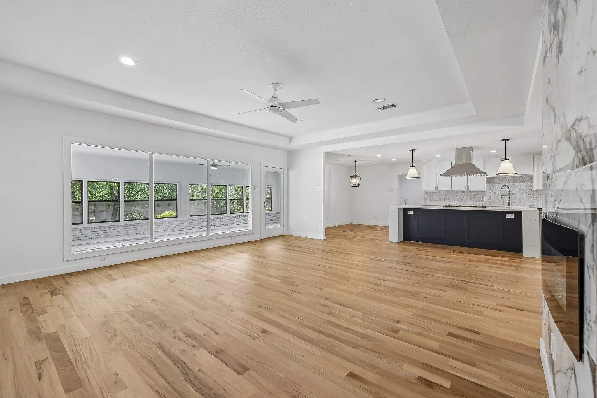 Open concept living area featuring wood-finish flooring, a contemporary fireplace with stone surround, recessed lighting, and a ceiling fan