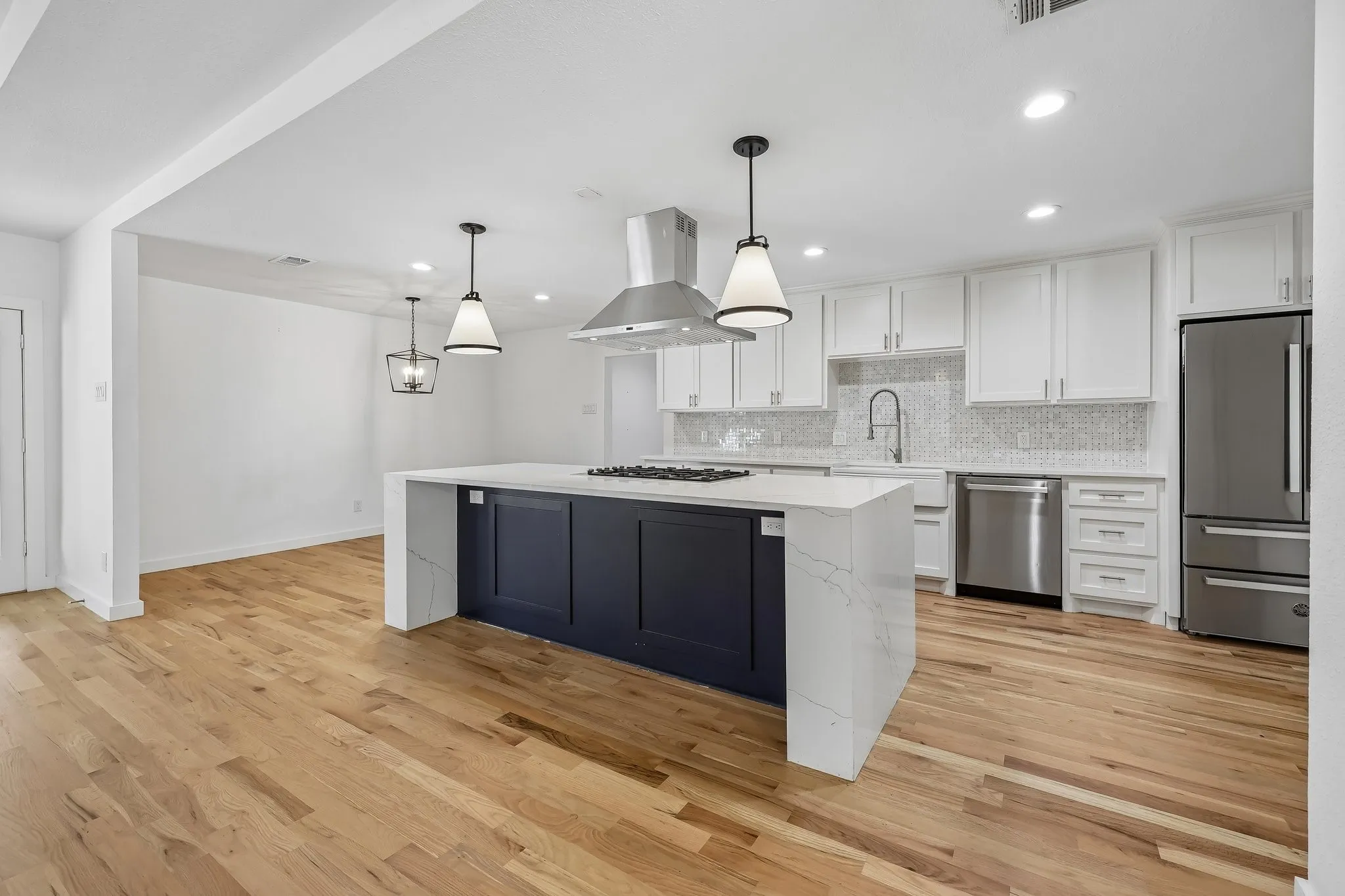 Spacious kitchen featuring an oversized island with cooktop, quartz countertops, white shaker cabinetry, stainless steel appliances, and wood-finish flooring