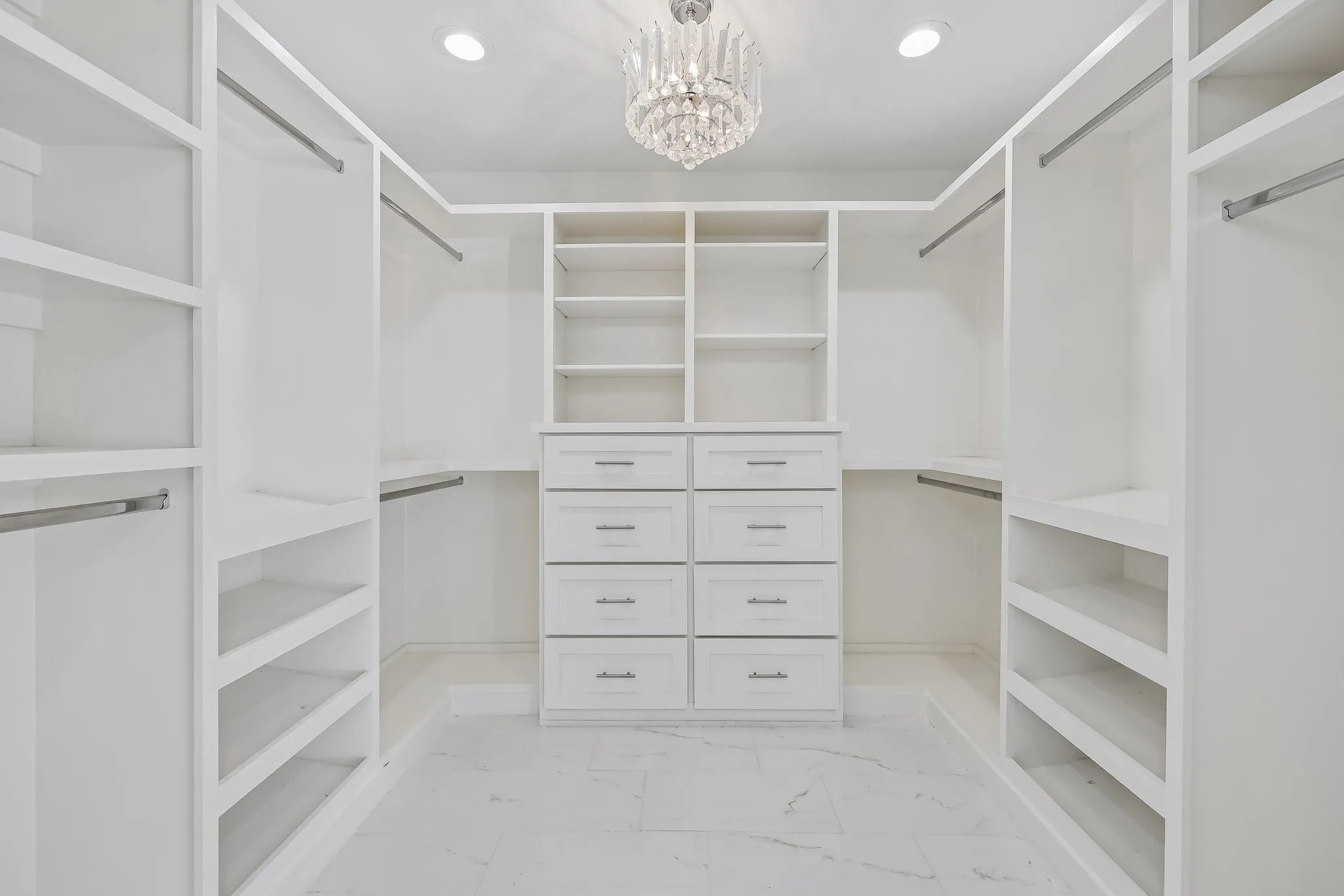Walk-in closet featuring white built-in shelving, hanging rods, and a central dresser unit with drawers
