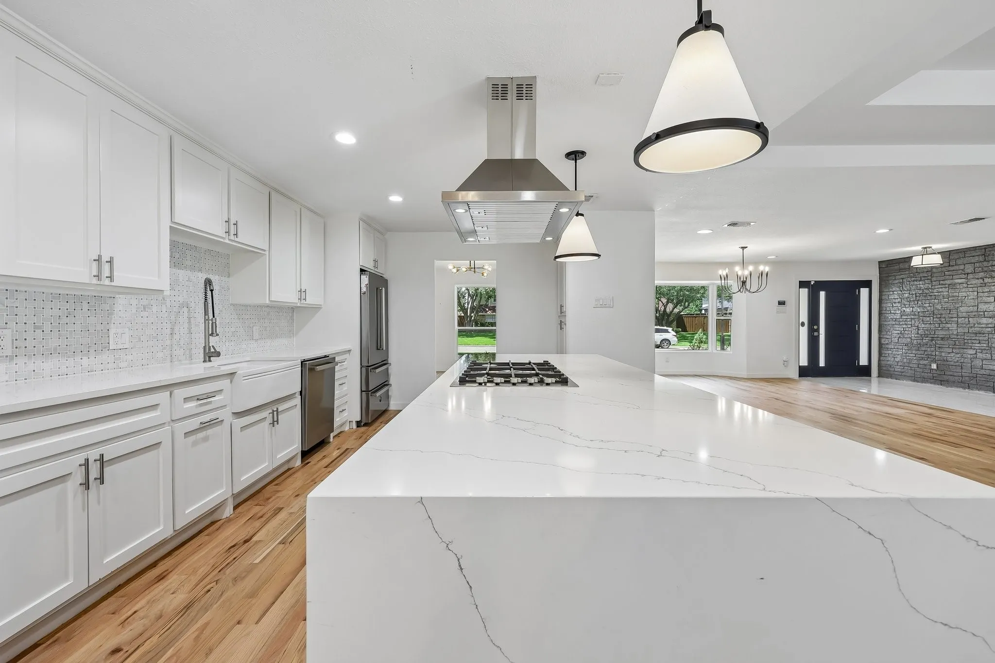 Contemporary kitchen featuring an oversized island with cooktop, white shaker cabinetry, stainless steel appliances, and wood-finish flooring