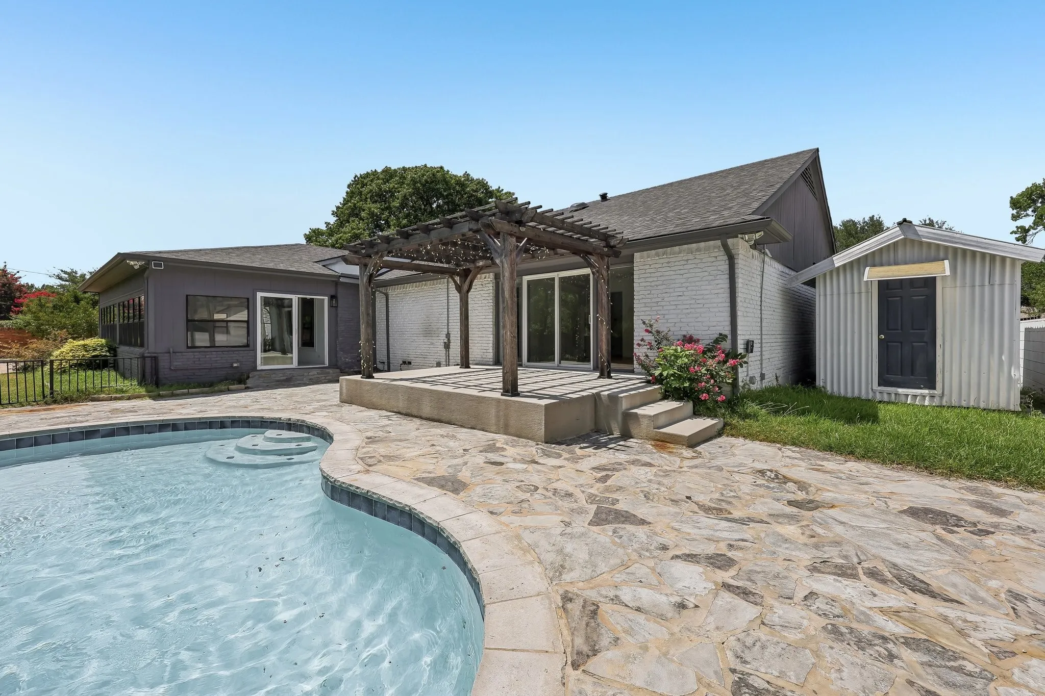 Outdoor space featuring a swimming pool with integrated steps, flagstone patio, and a wood pergola