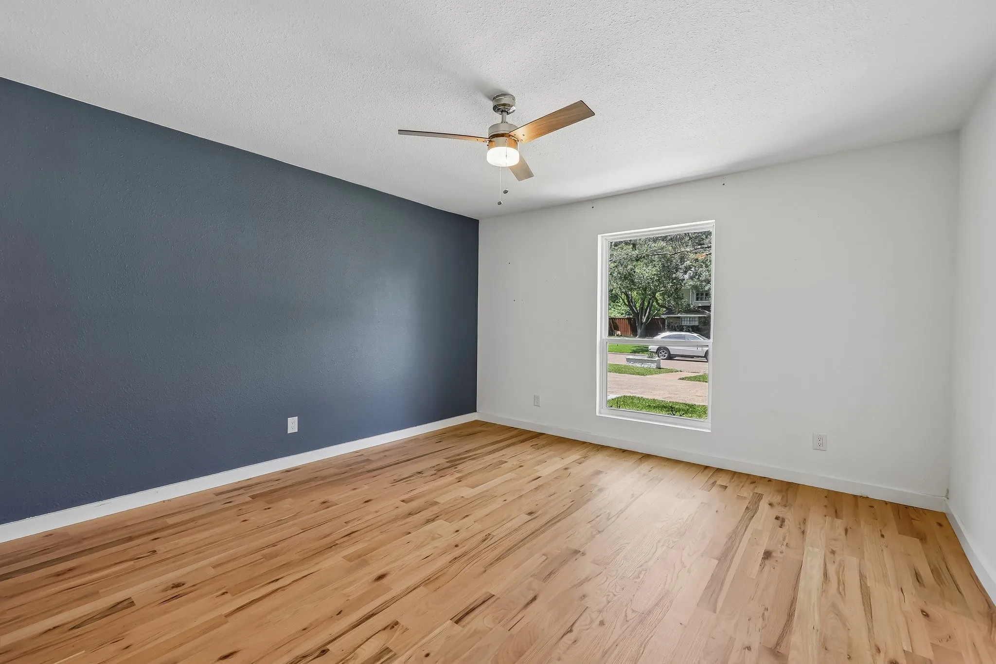 Spacious room featuring wood-finish flooring, a contemporary ceiling fan with lighting, and a large window
