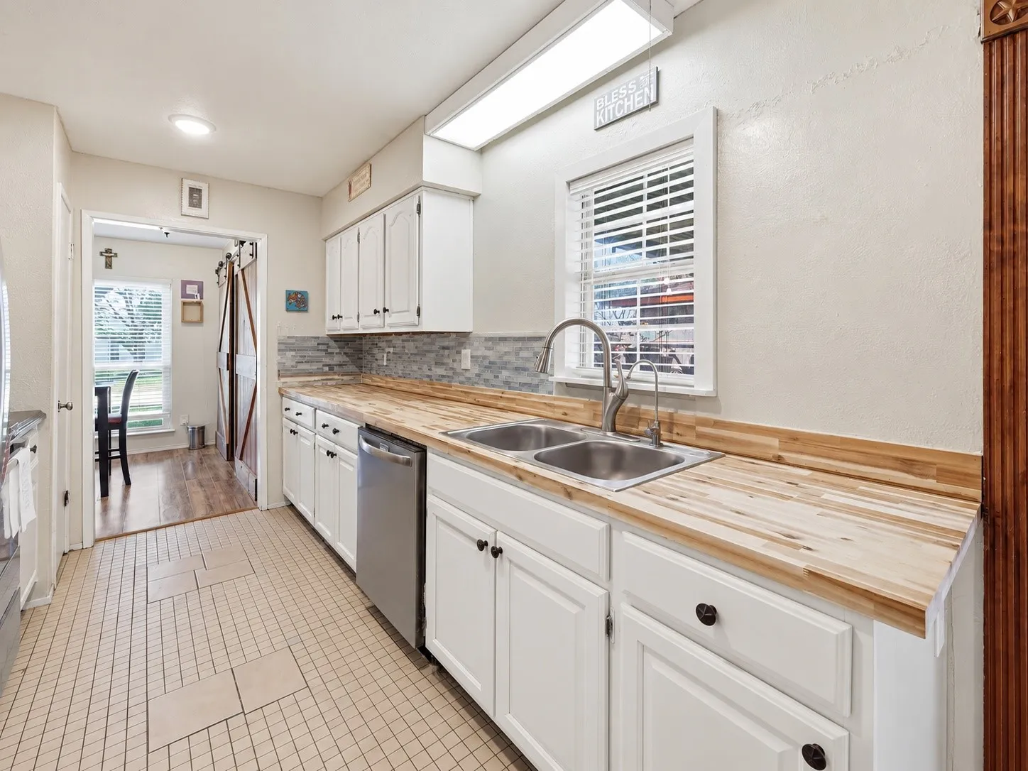 White cabinetry with dark hardware, wood-finish countertops, stainless steel sink, tiled backsplash, and recessed lighting