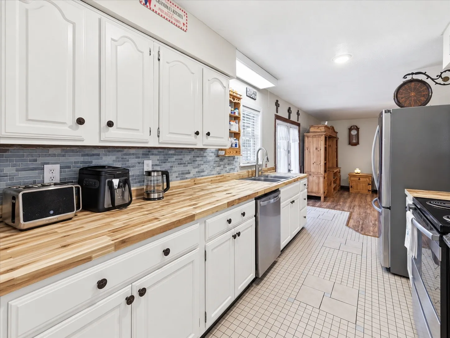 White cabinetry, wood-finish countertops, stainless steel sink, tile backsplash, and tile flooring