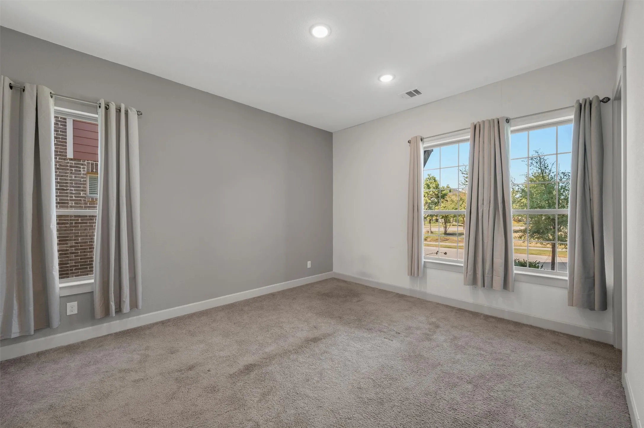 Recessed ceiling lighting, textured carpeting, multiple windows, and a gray accent wall