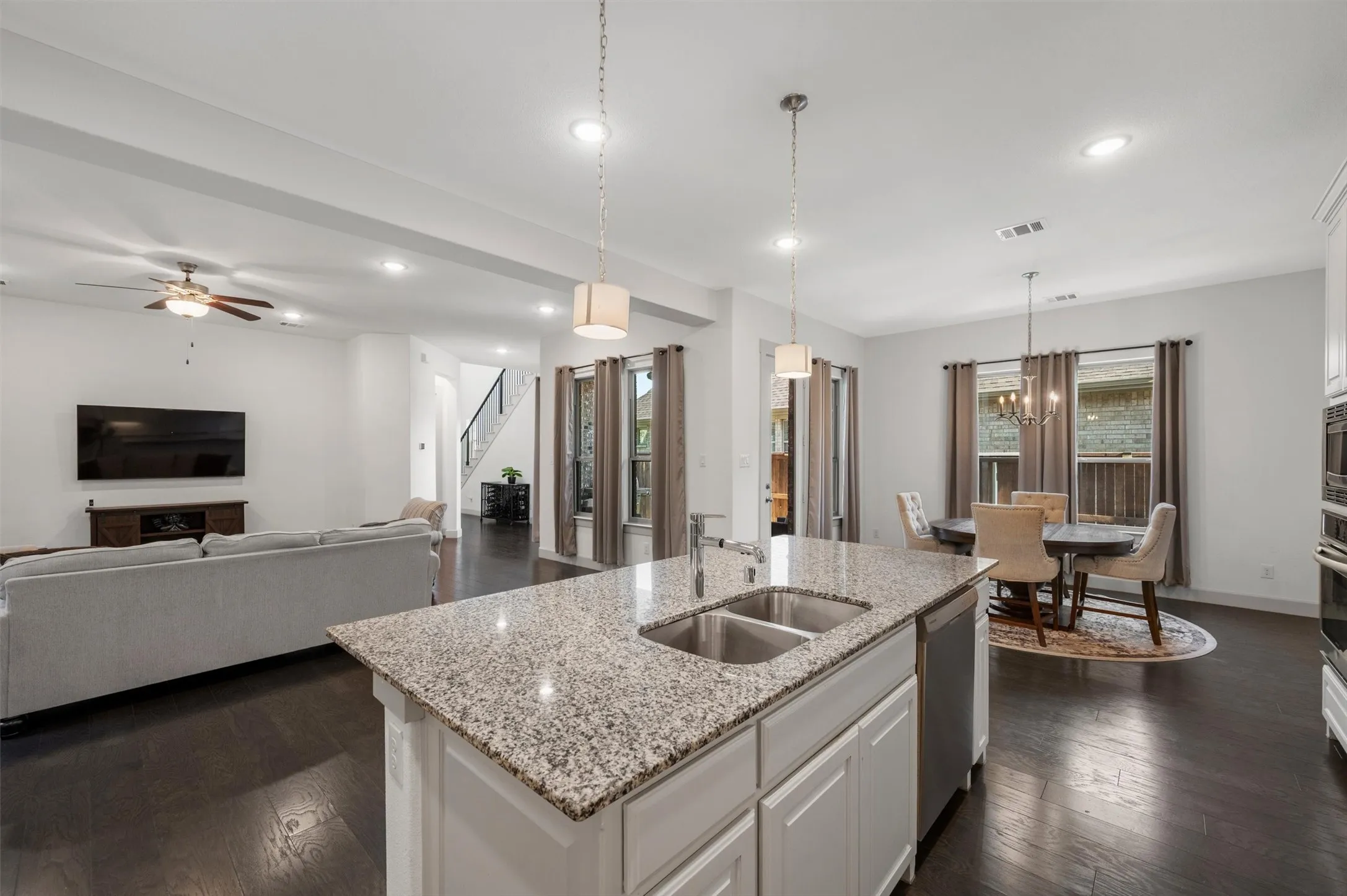 Open-concept living space featuring wood-finish flooring, a kitchen island with stone countertop and double basin sink, recessed lighting, and a dining area with chandelier