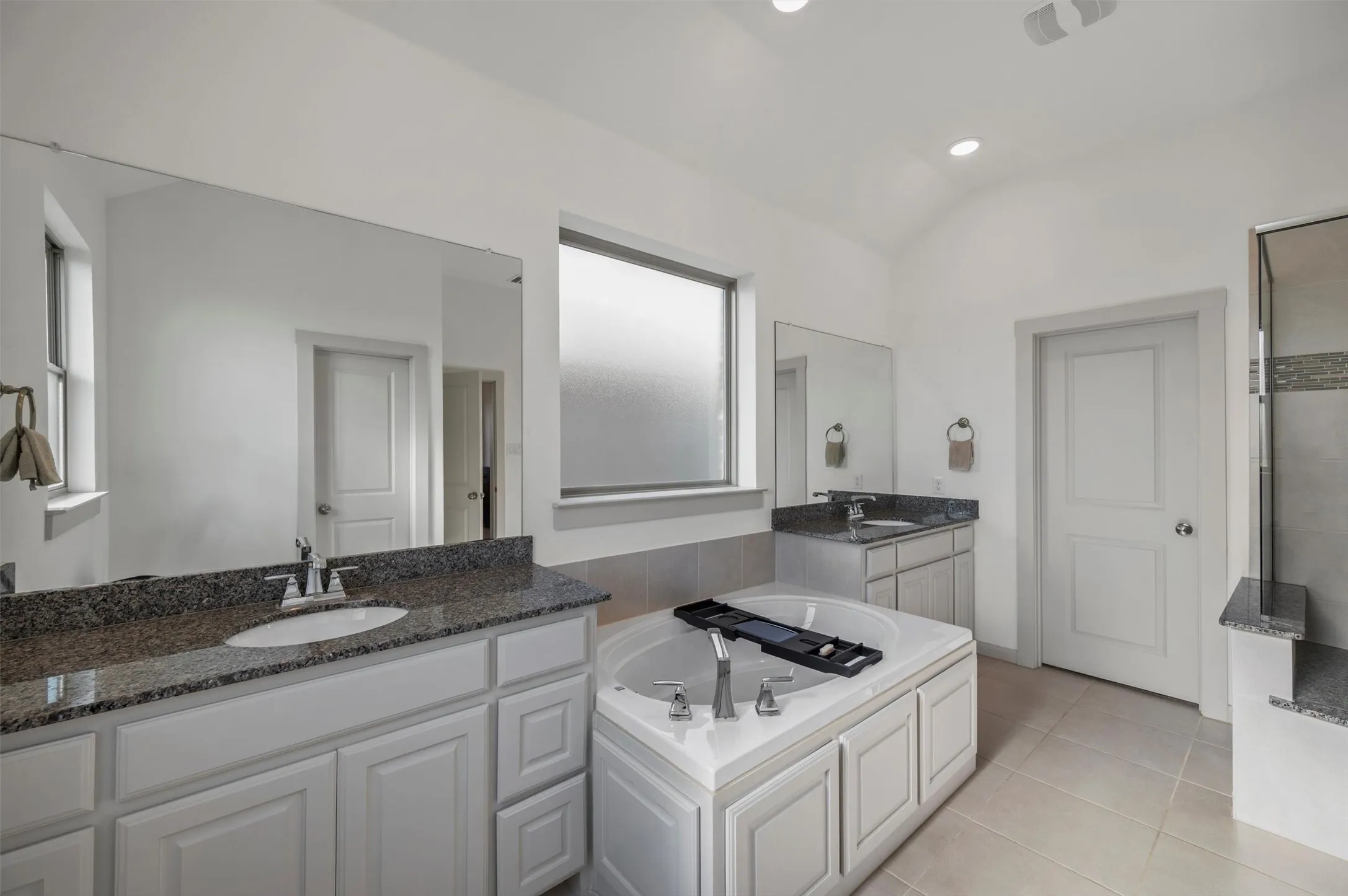 Bathroom featuring dual vanity with granite countertops, integrated drop-in sinks, a built-in soaking tub, and a separate shower with tiled walls