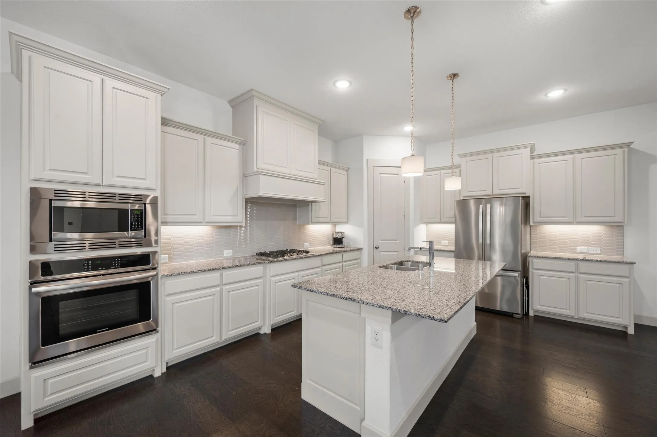 Gourmet kitchen with white cabinetry, stainless steel appliances, speckled stone countertops, a central island with an undermount sink, and dark wood-finish flooring
