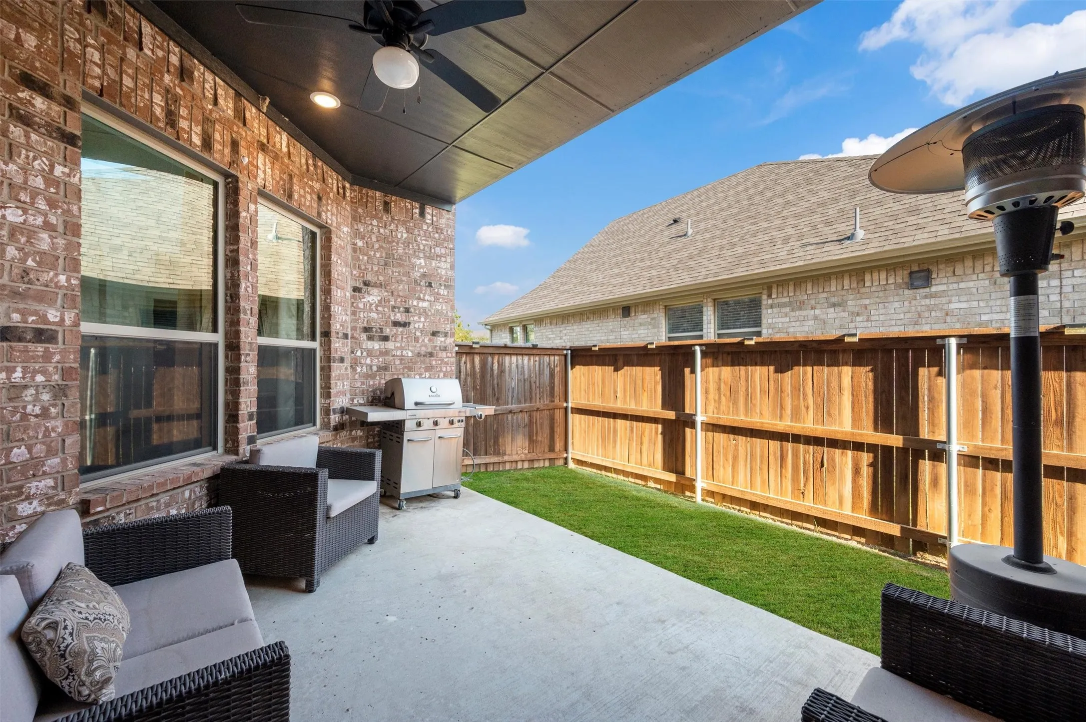 Covered patio with a ceiling fan, brick exterior, concrete patio surface, and a private wooden fence