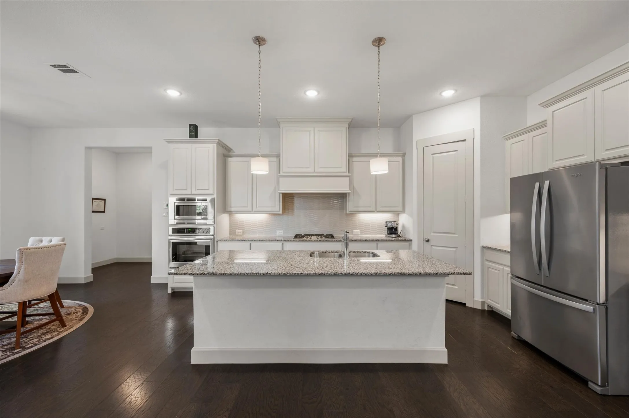 Kitchen featuring a central island with a sink, white cabinetry, integrated stainless steel appliances, and dark wood-finish flooring