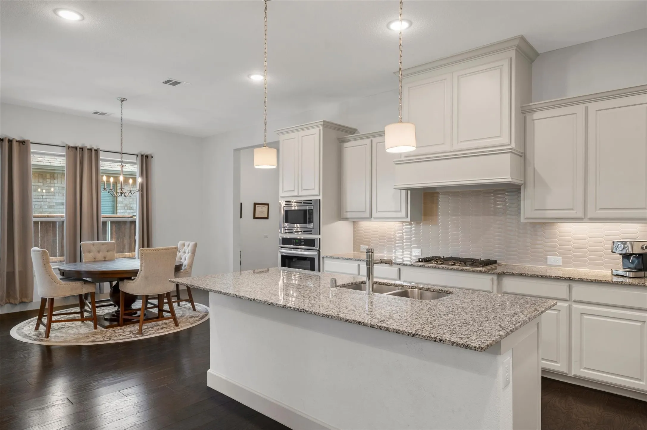 Kitchen featuring a center island with sink, white shaker-style cabinetry, double wall ovens, a gas cooktop, and a tile backsplash