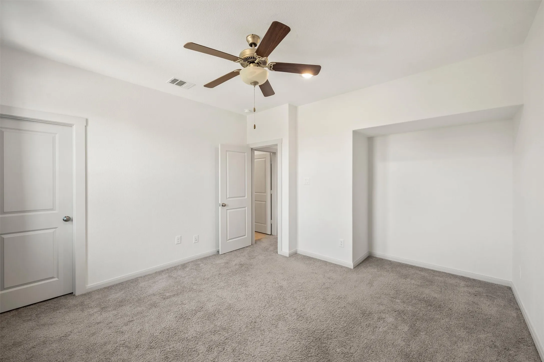 Carpeted room with a ceiling fan, recessed wall alcove, and a paneled door