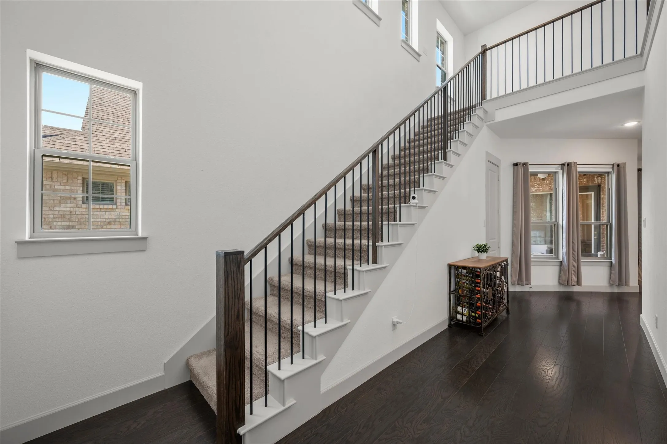Two-story entryway featuring wood-finish flooring, a carpeted staircase with dark wood-finish handrails and black metal balusters, and multiple windows
