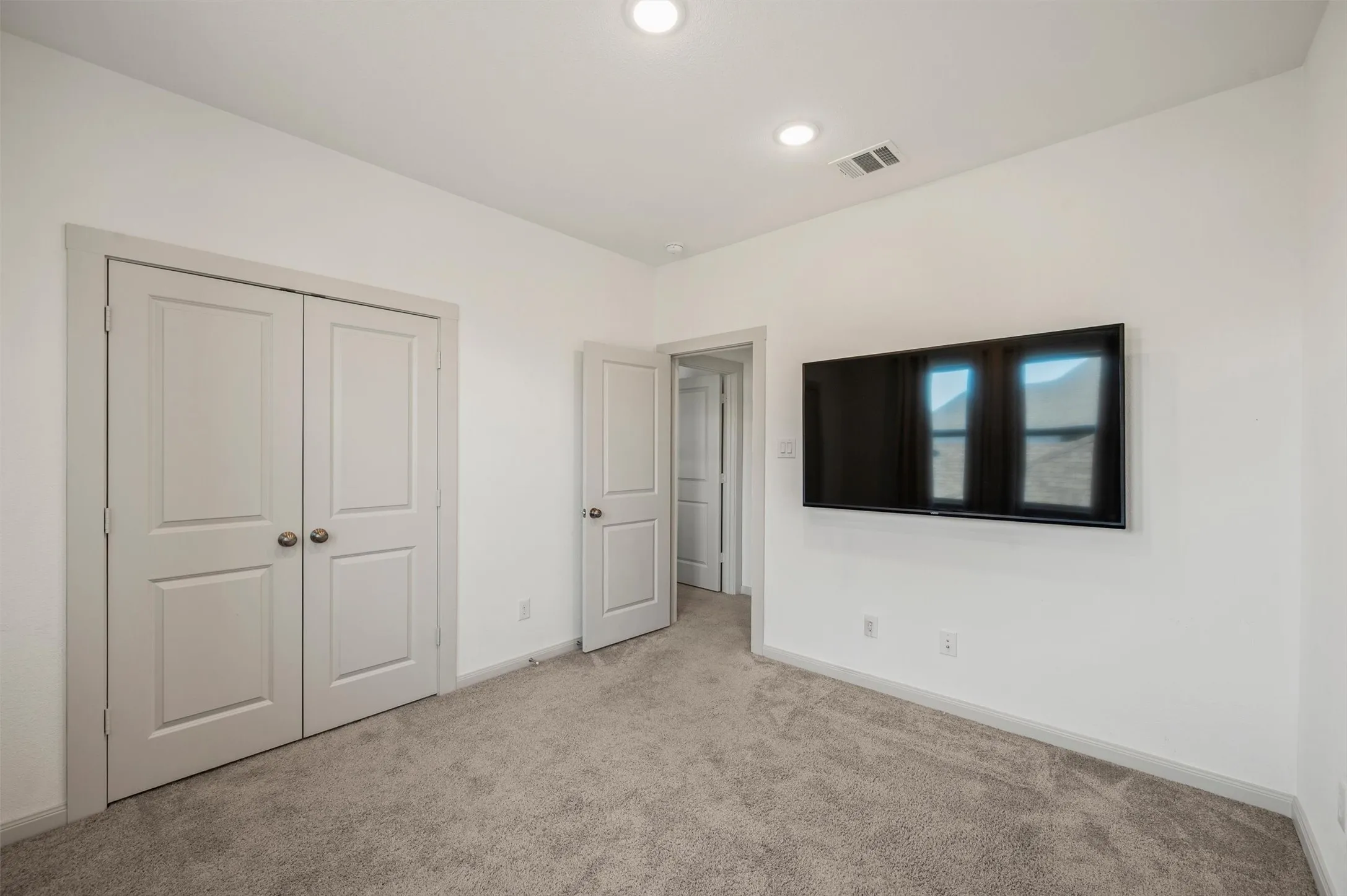 Wall-mounted television, recessed lighting, double panel doors, and gray carpeting