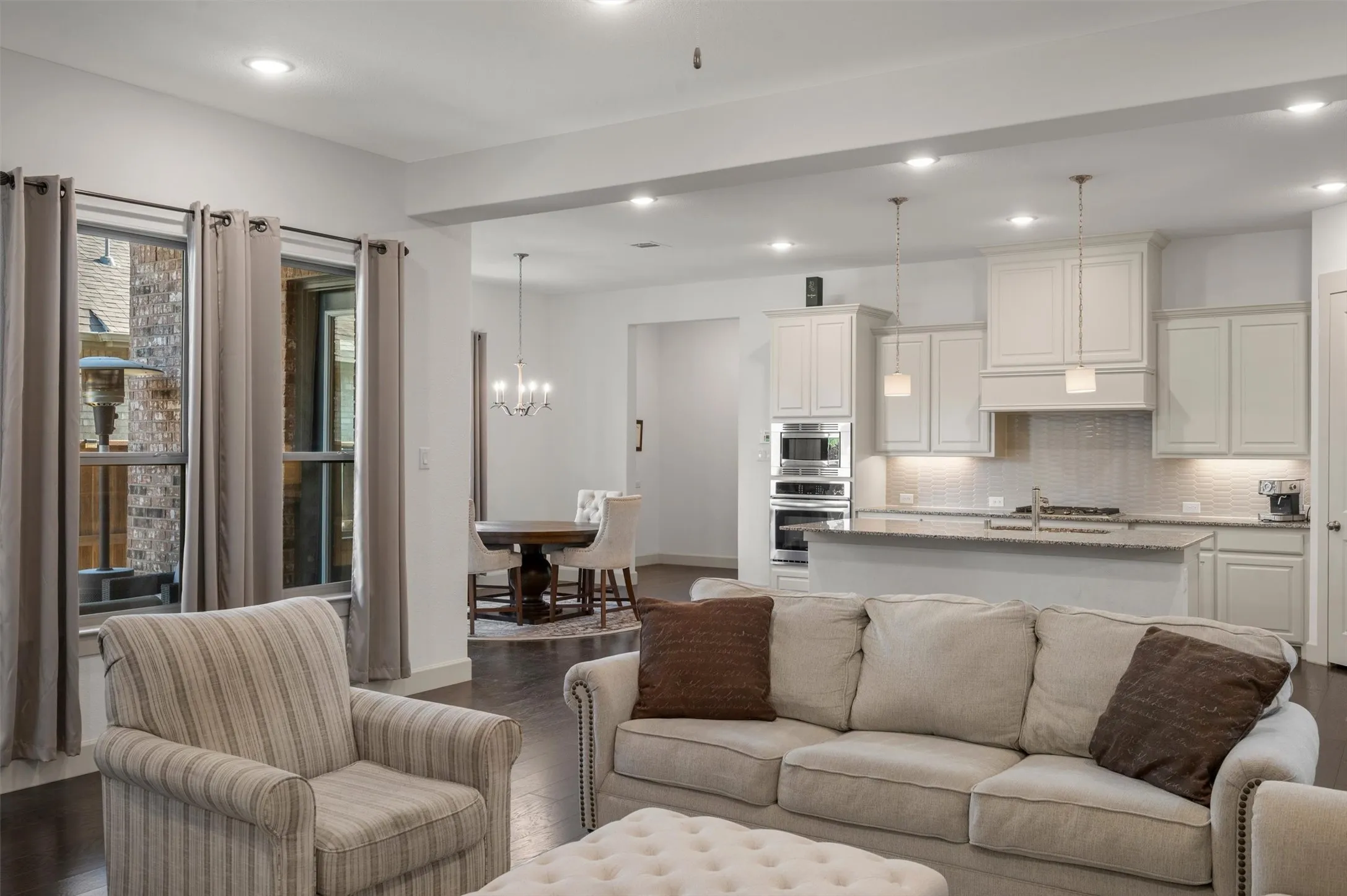 Open-concept living space featuring wood-finish flooring, recessed lighting, and a kitchen with white cabinetry, built-in stainless steel appliances, and a central island with a stone countertop