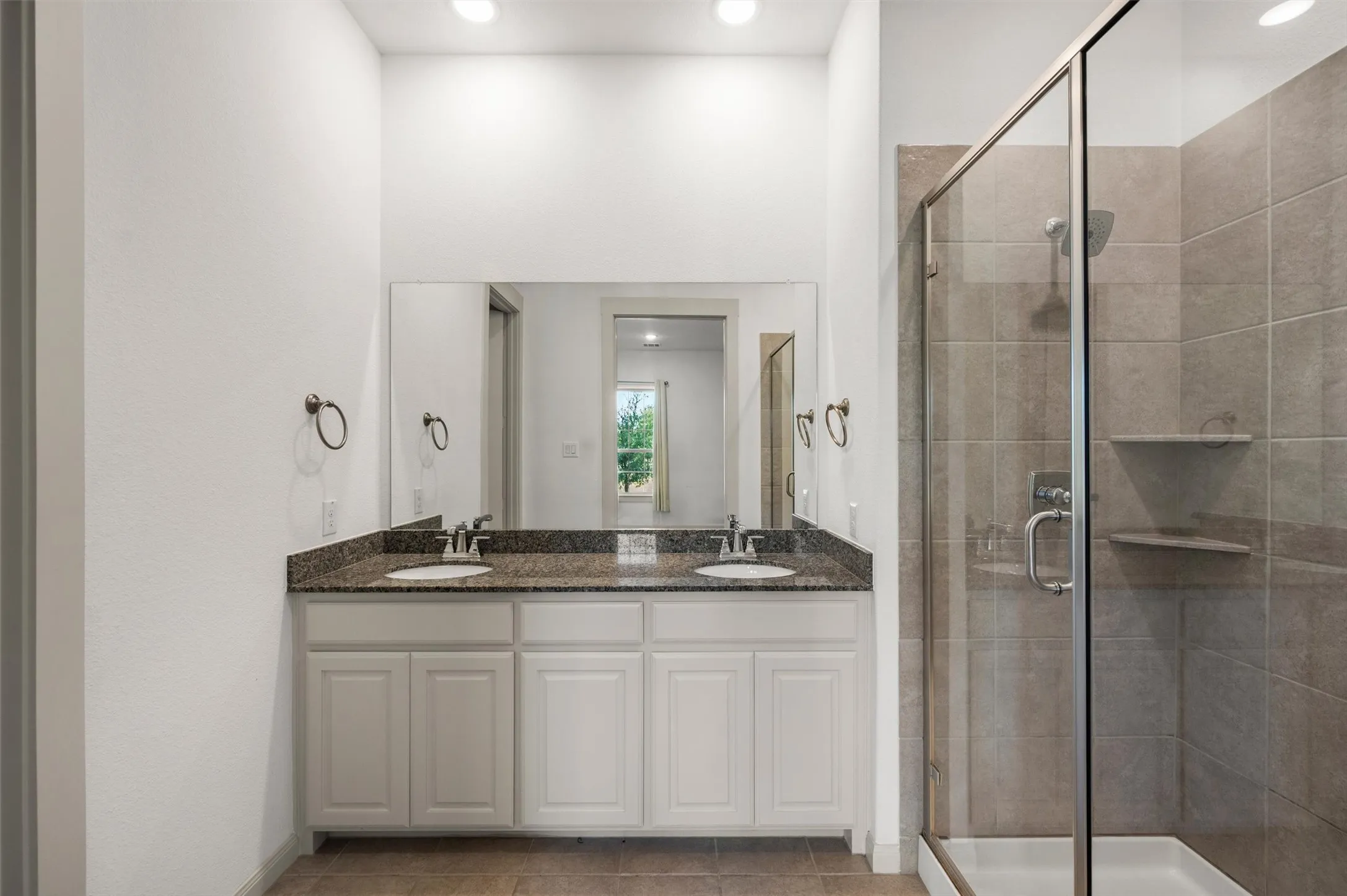 Dual vanity with granite countertop, individual basin sinks, and a glass-enclosed shower with tiled walls and built-in shelving