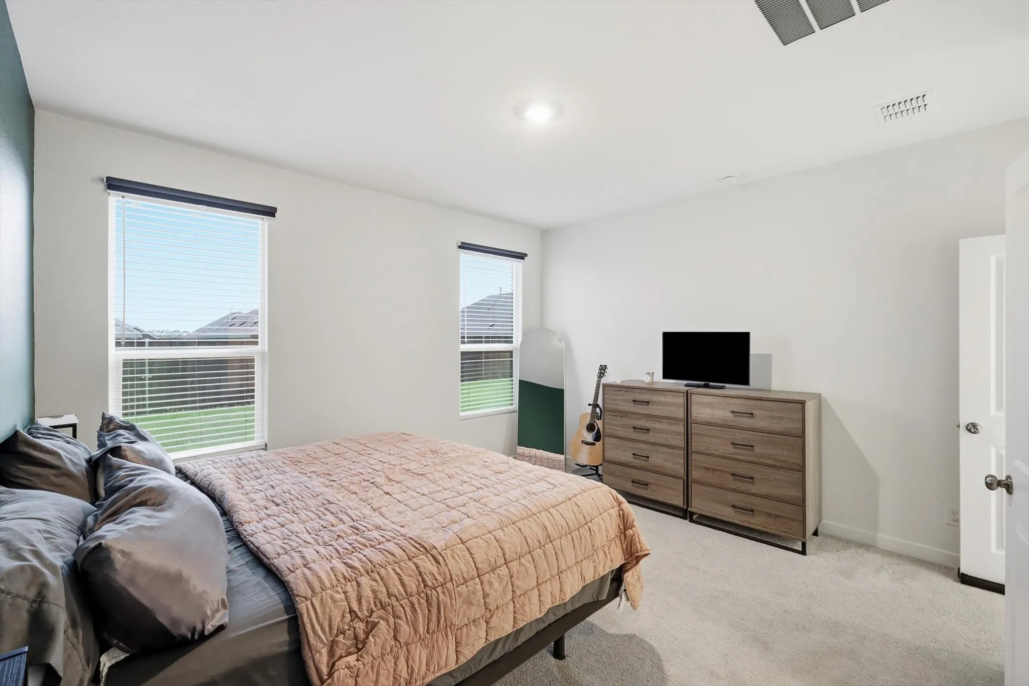 Bright bedroom featuring plush carpet flooring and two windows with blinds
