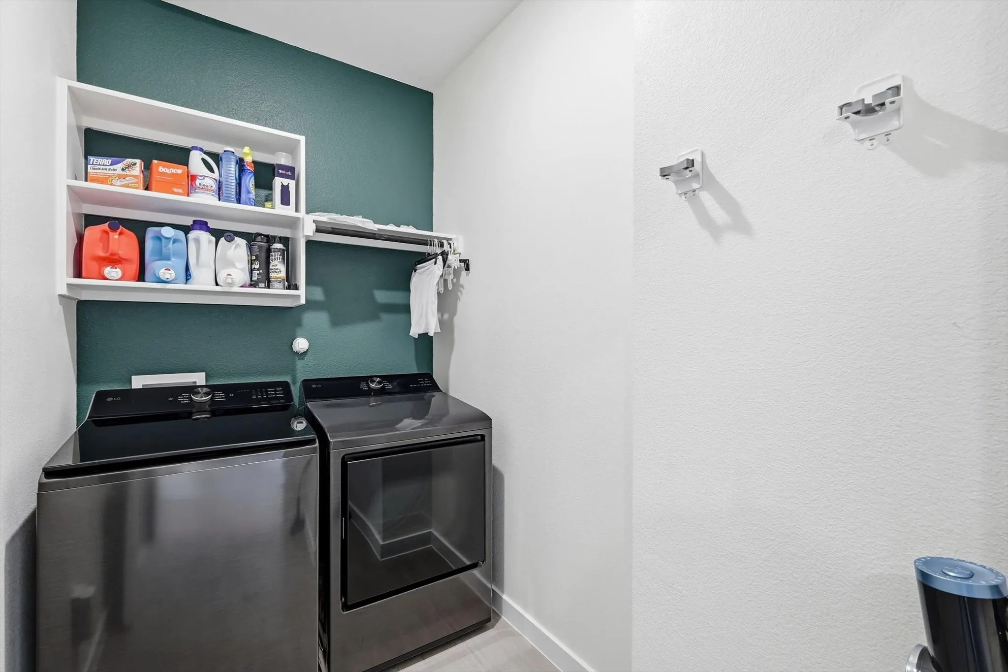 Laundry area featuring modern front-loading appliances, white shelving, and a wall-mounted hanging rod
