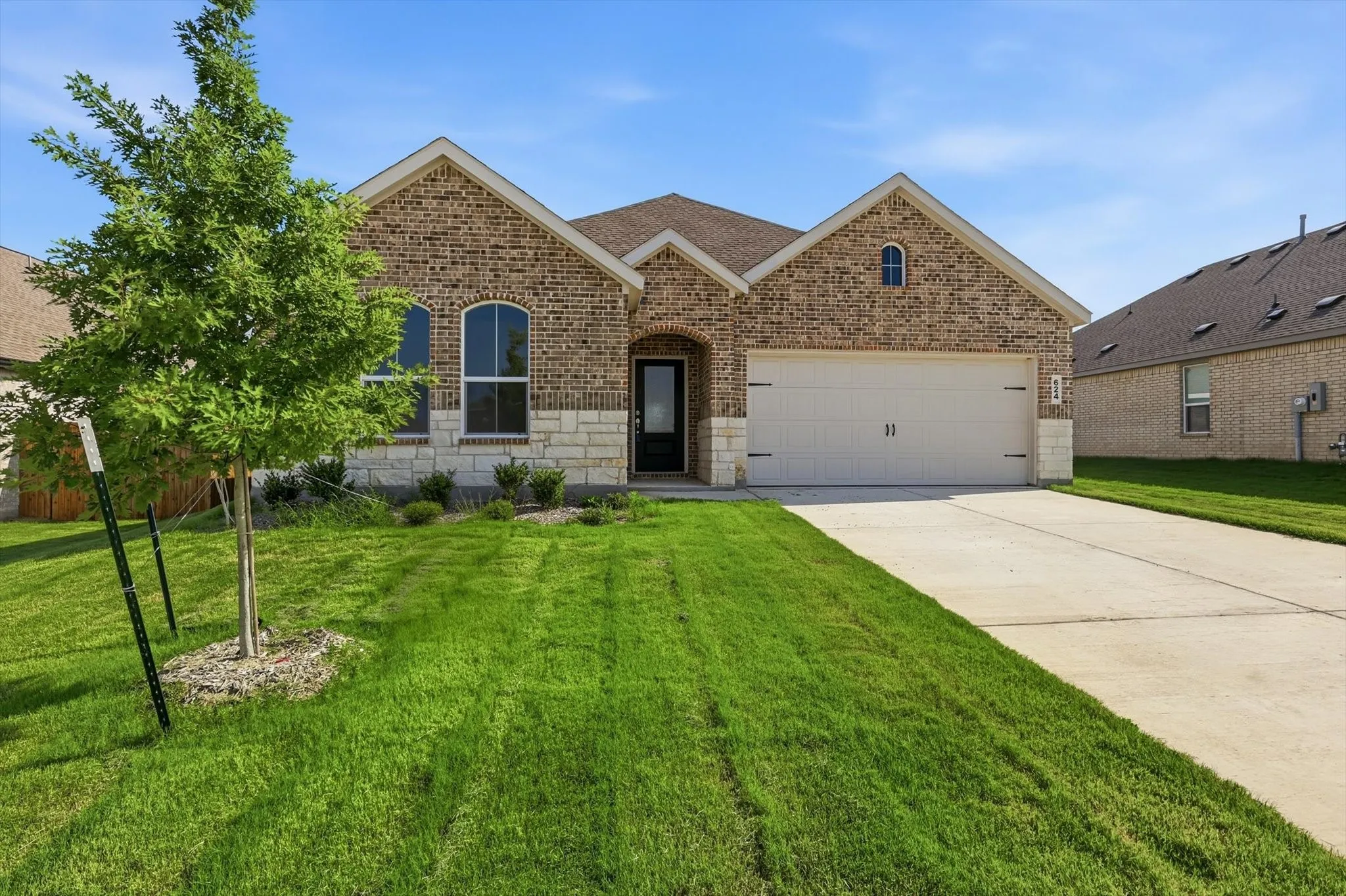 Brick facade featuring stone accents, arched windows, an attached two-car garage, and a concrete driveway