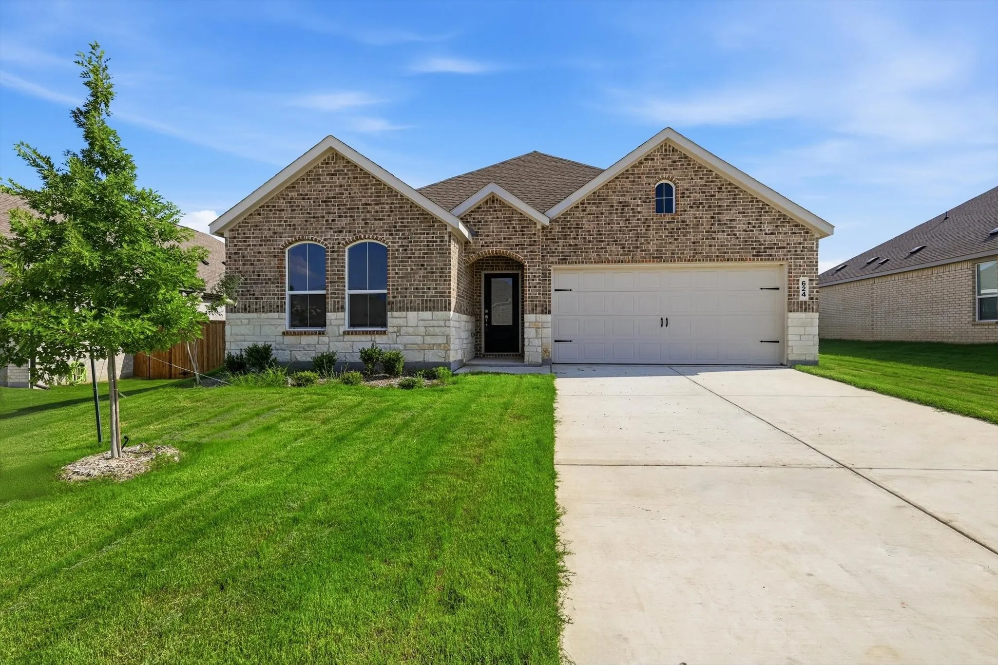 Brick and stone facade featuring a two-car garage, arched windows, and a concrete driveway