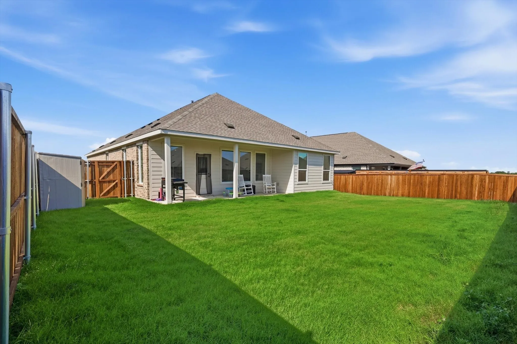 Expansive backyard featuring a lush lawn, privacy fencing, and a covered patio area