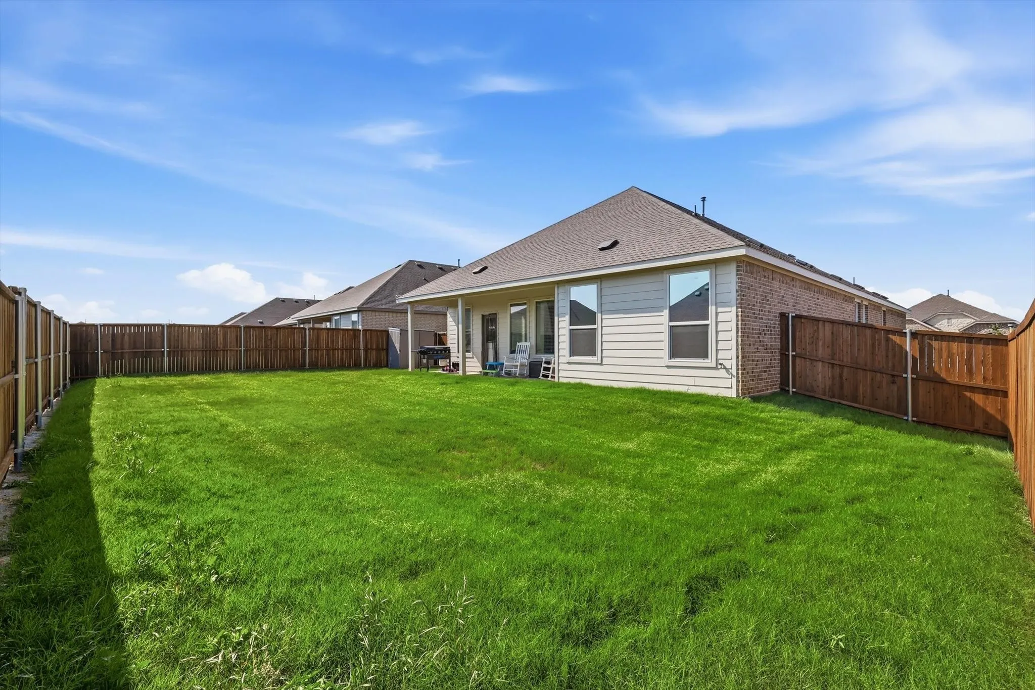 Expansive backyard featuring a manicured lawn, full wood privacy fencing, and a covered patio area with a concrete slab