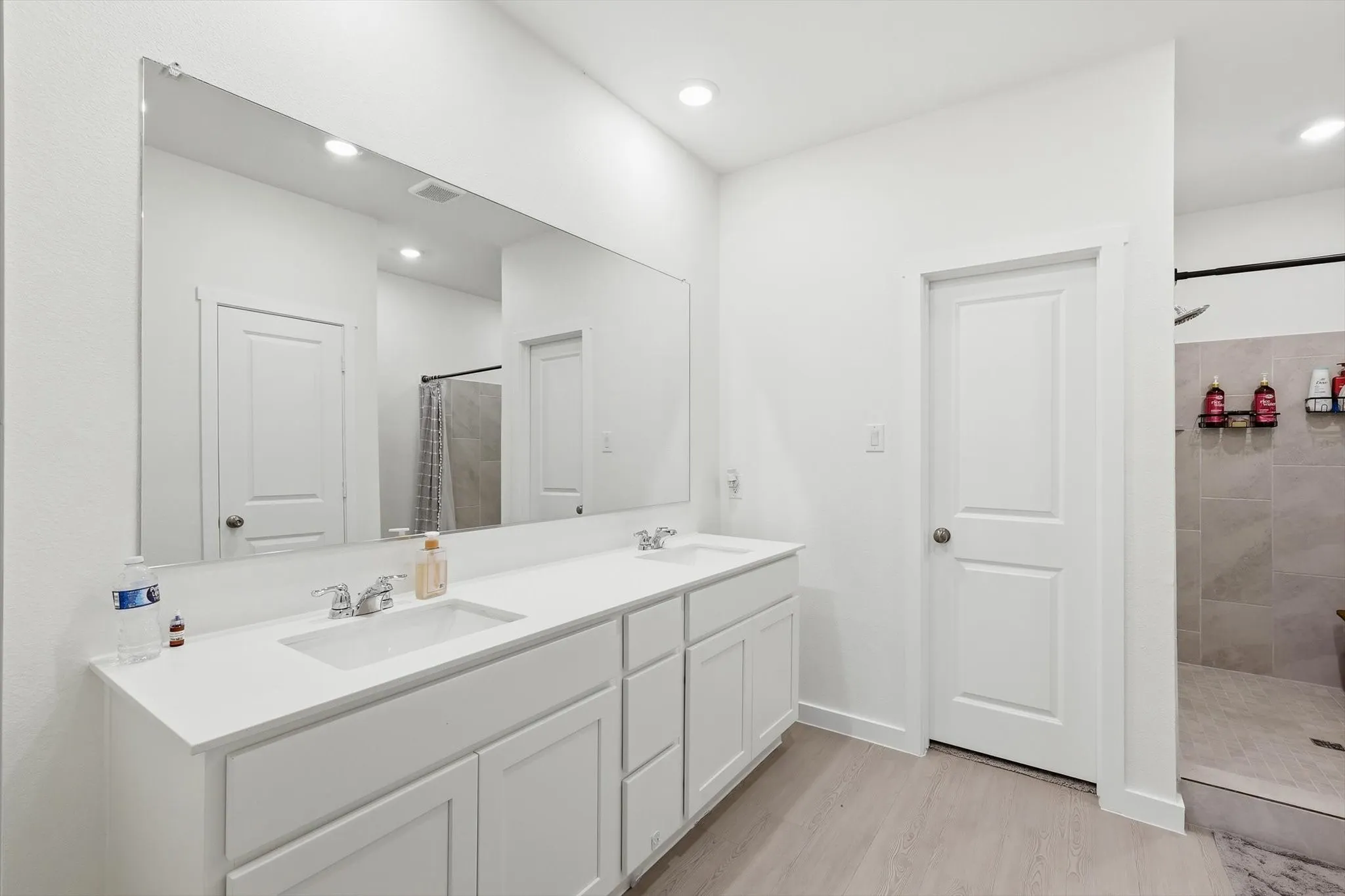Bathroom featuring a dual vanity with white cabinetry and integrated sinks, a large wall-mounted mirror, recessed lighting, and light wood-finish flooring
