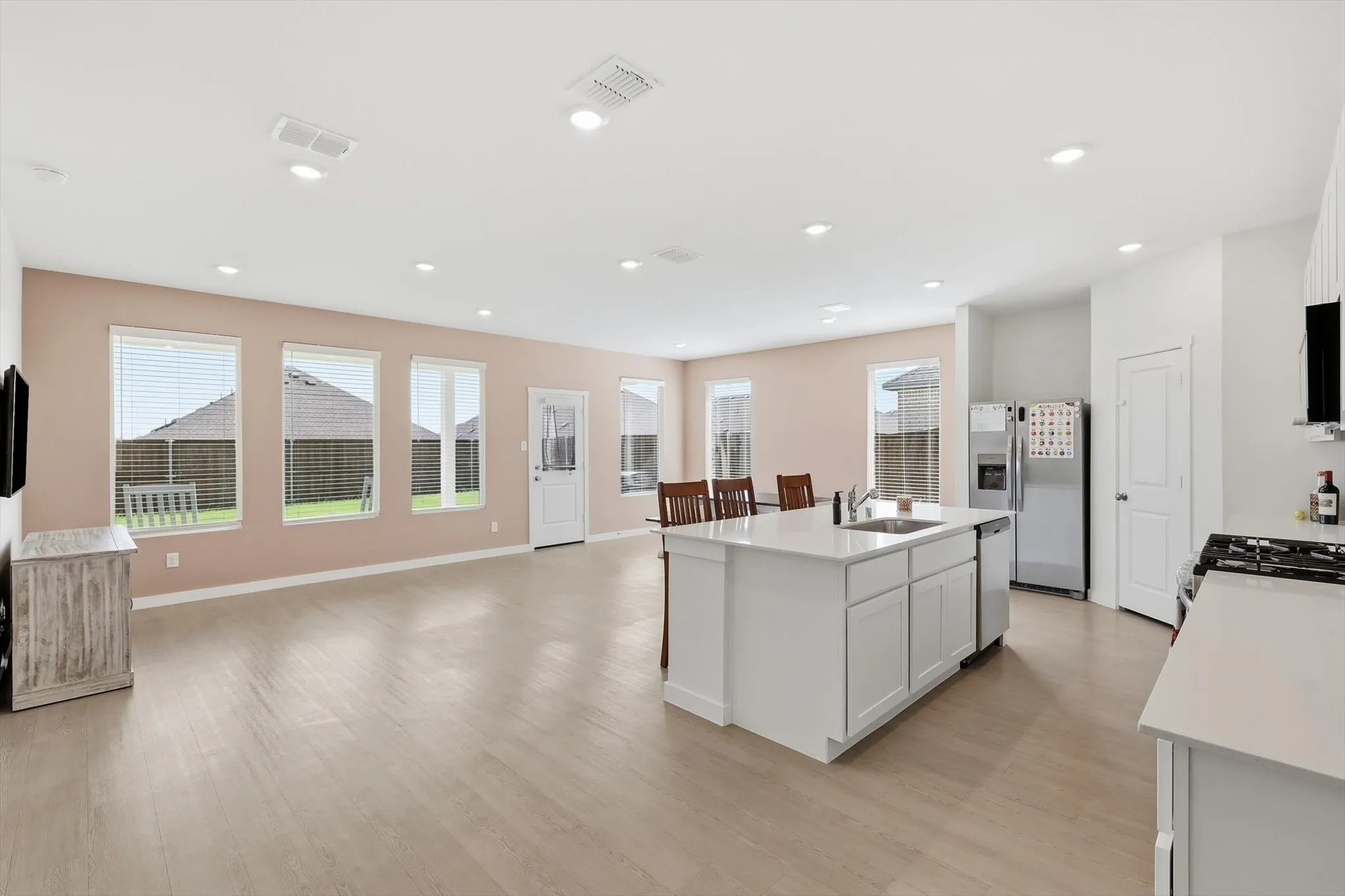 Open-concept living space featuring wood-finish flooring, recessed lighting, and a kitchen island with integrated sink