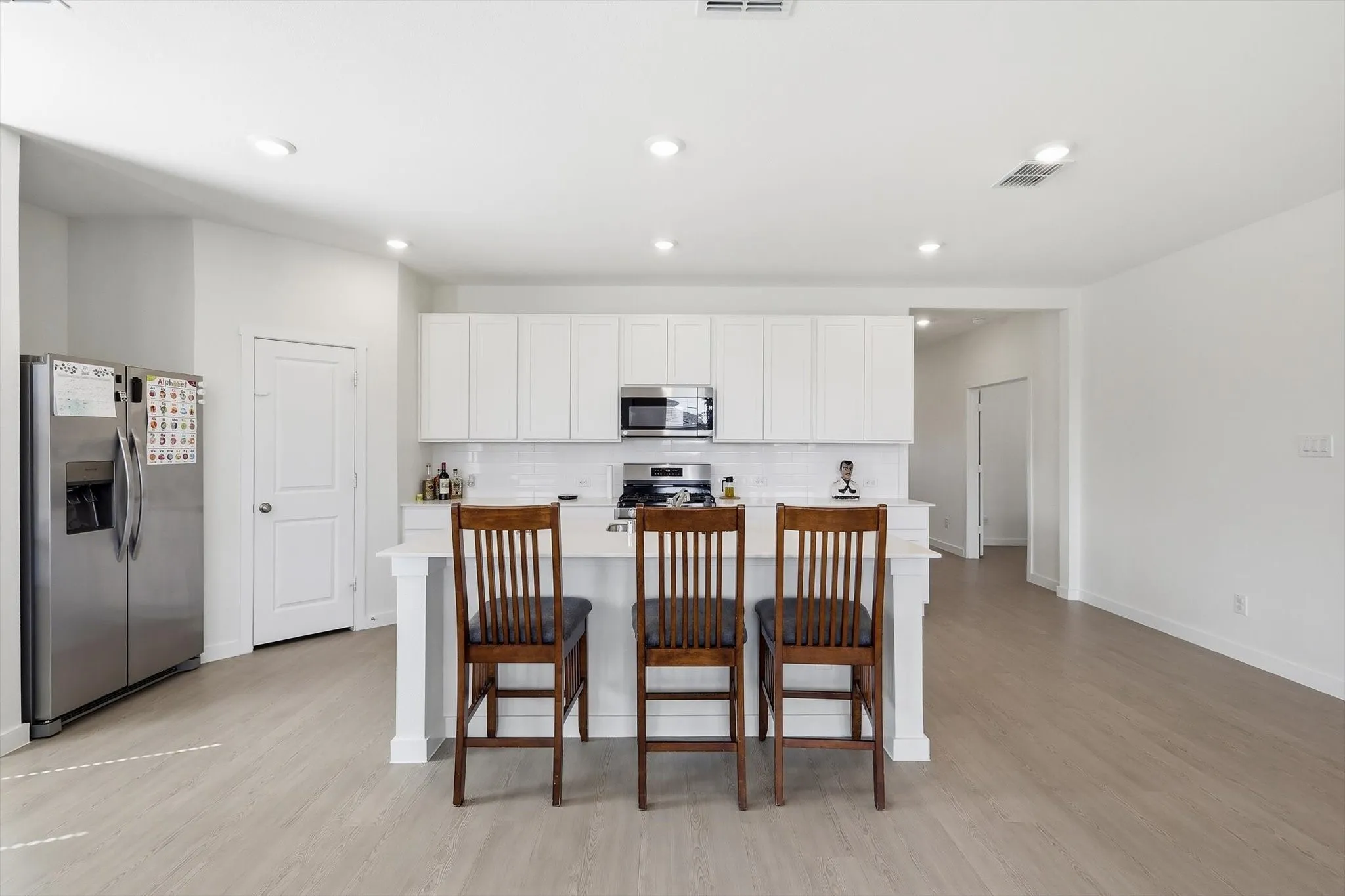 Bright kitchen featuring a central island with seating, white cabinetry, stainless steel appliances, and a subway tile backsplash