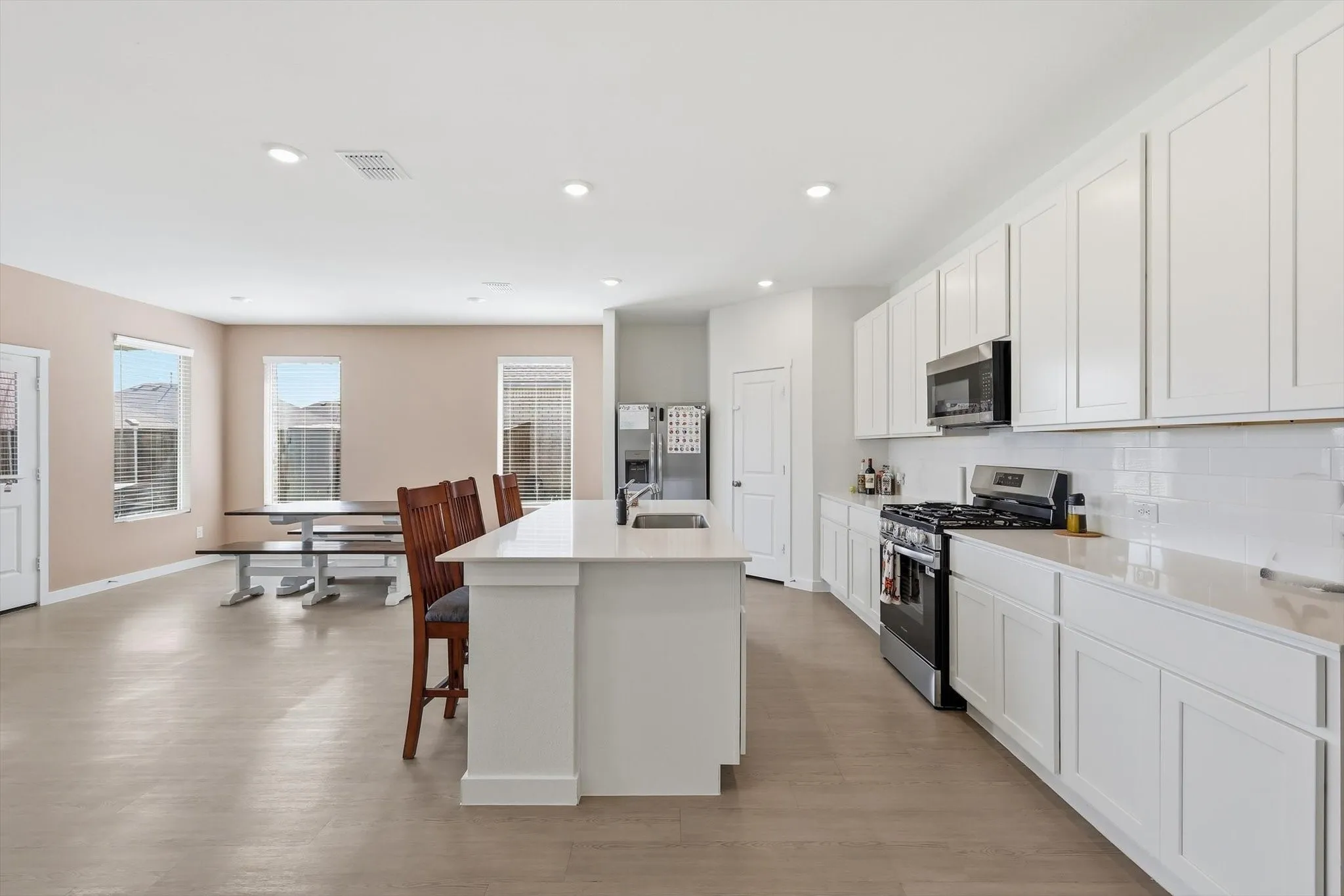 Open-concept kitchen featuring an eat-in island, white cabinetry, a gas range, stainless steel appliances, and a subway tile backsplash
